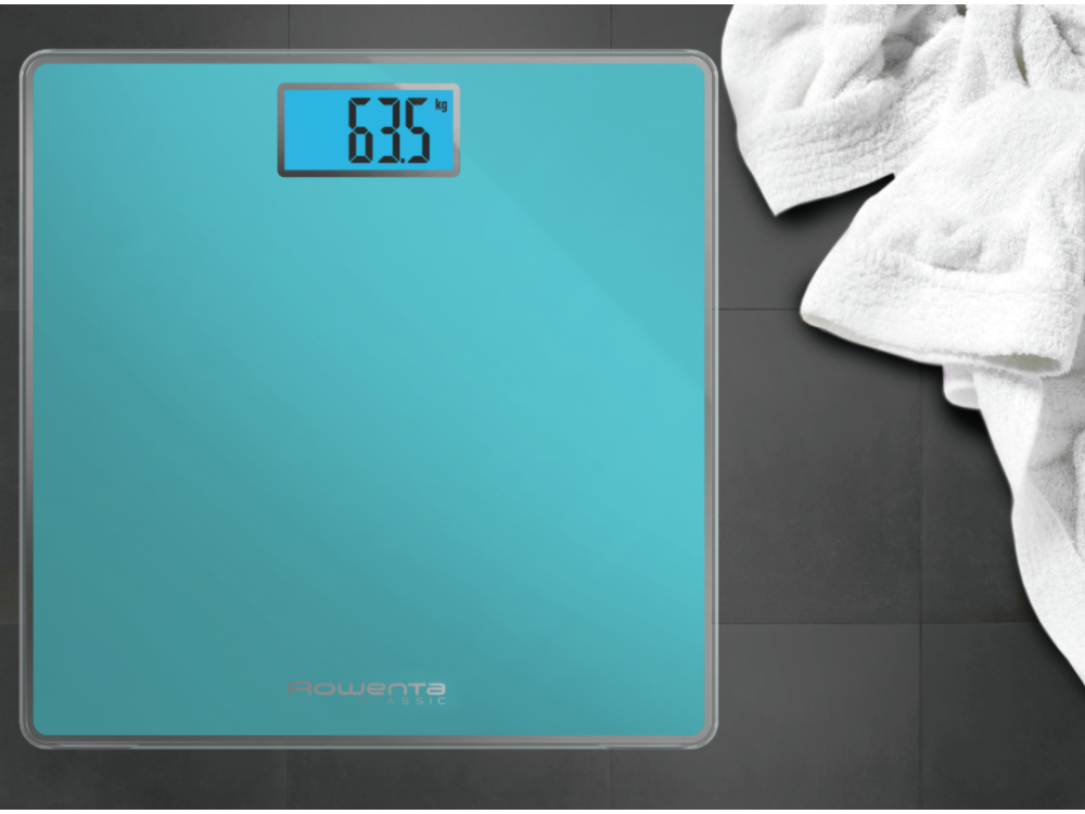 Báscula digital turquesa que muestra 63,5 kg, con una toalla blanca sobre un suelo de baldosas oscuras.