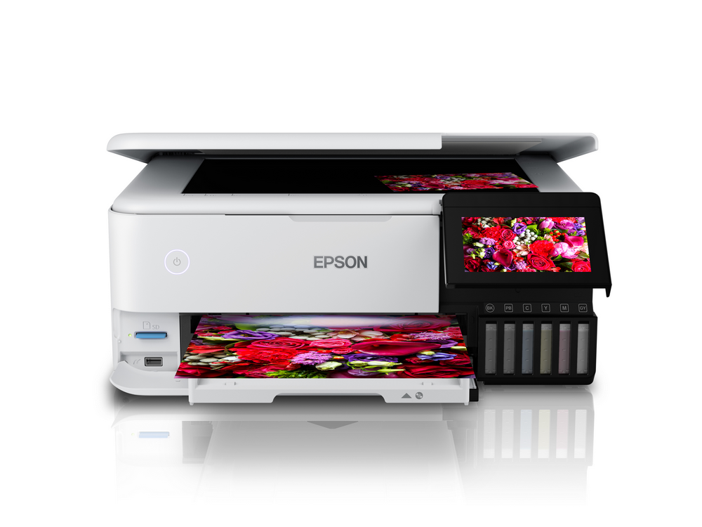 Impresora blanca con una pantalla que muestra flores. Múltiples depósitos de tinta y fondo blanco.