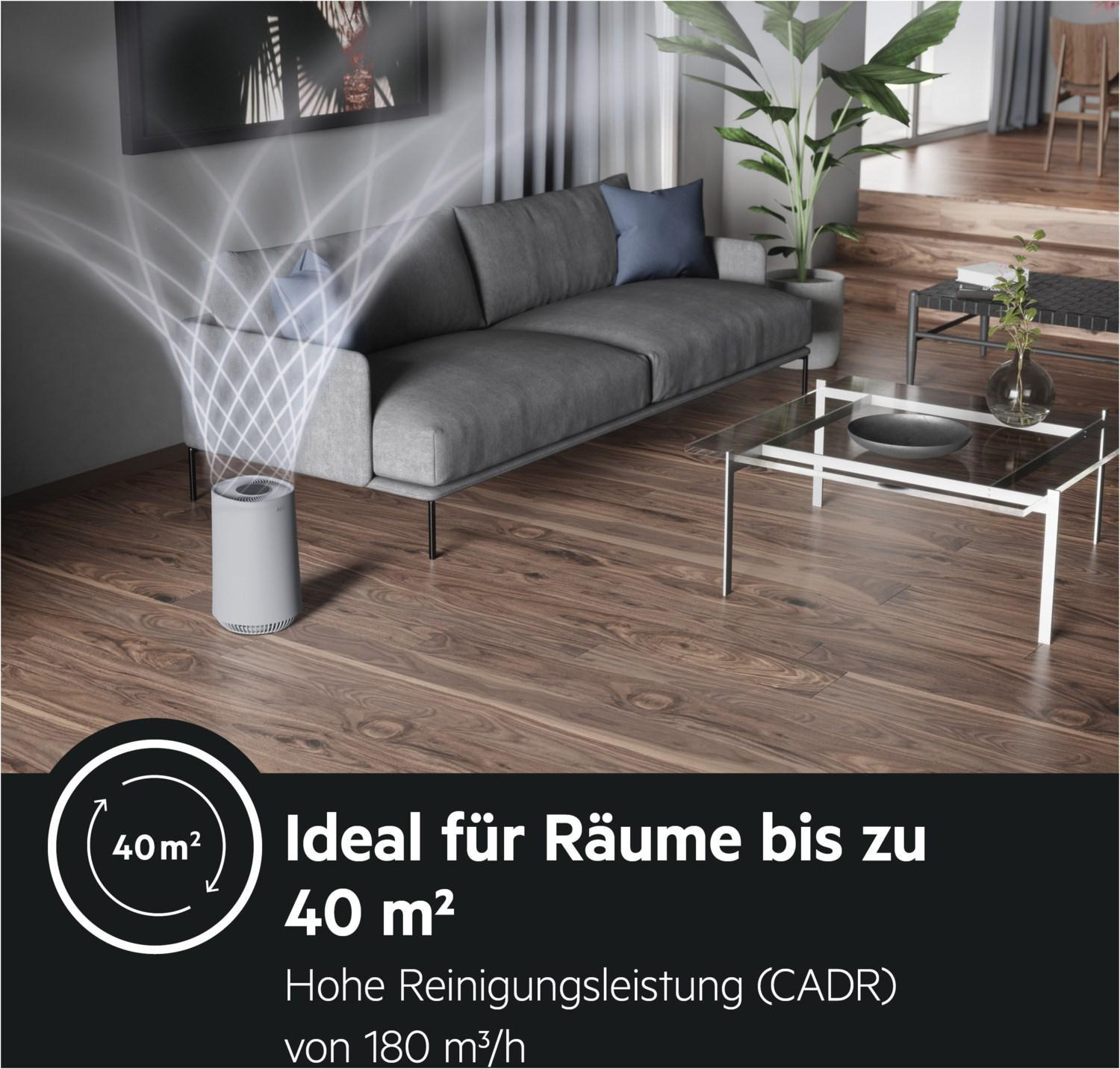 Luftreiniger in einem Wohnzimmer. Graues Sofa, Holzboden und Pflanze im Hintergrund.