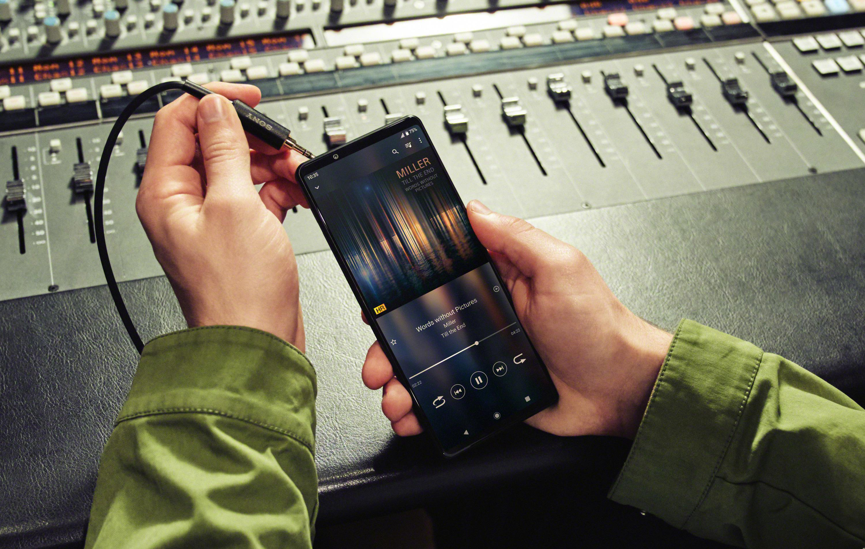 Hand hält Telefon an Mischpult. Das Telefon zeigt Musik an.