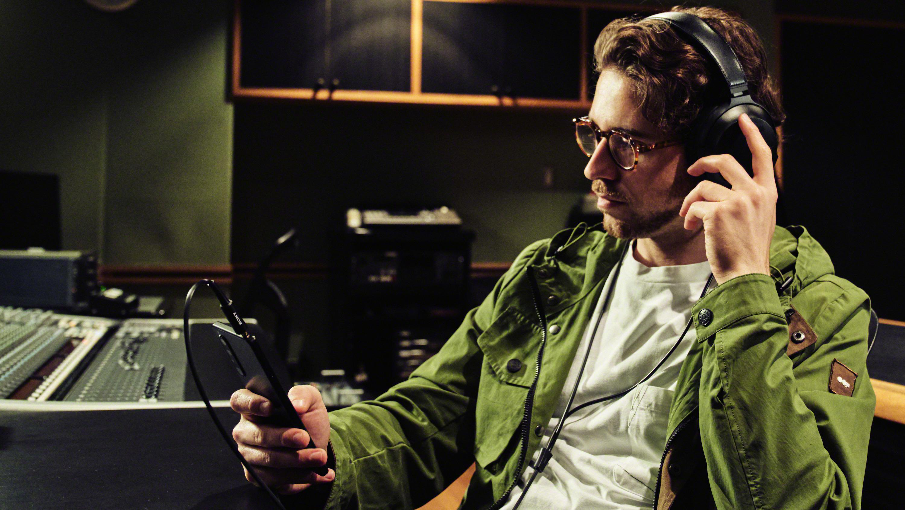 Ein Mann mit Kopfhörern und Brille, der in einem Studio auf ein Telefon schaut.