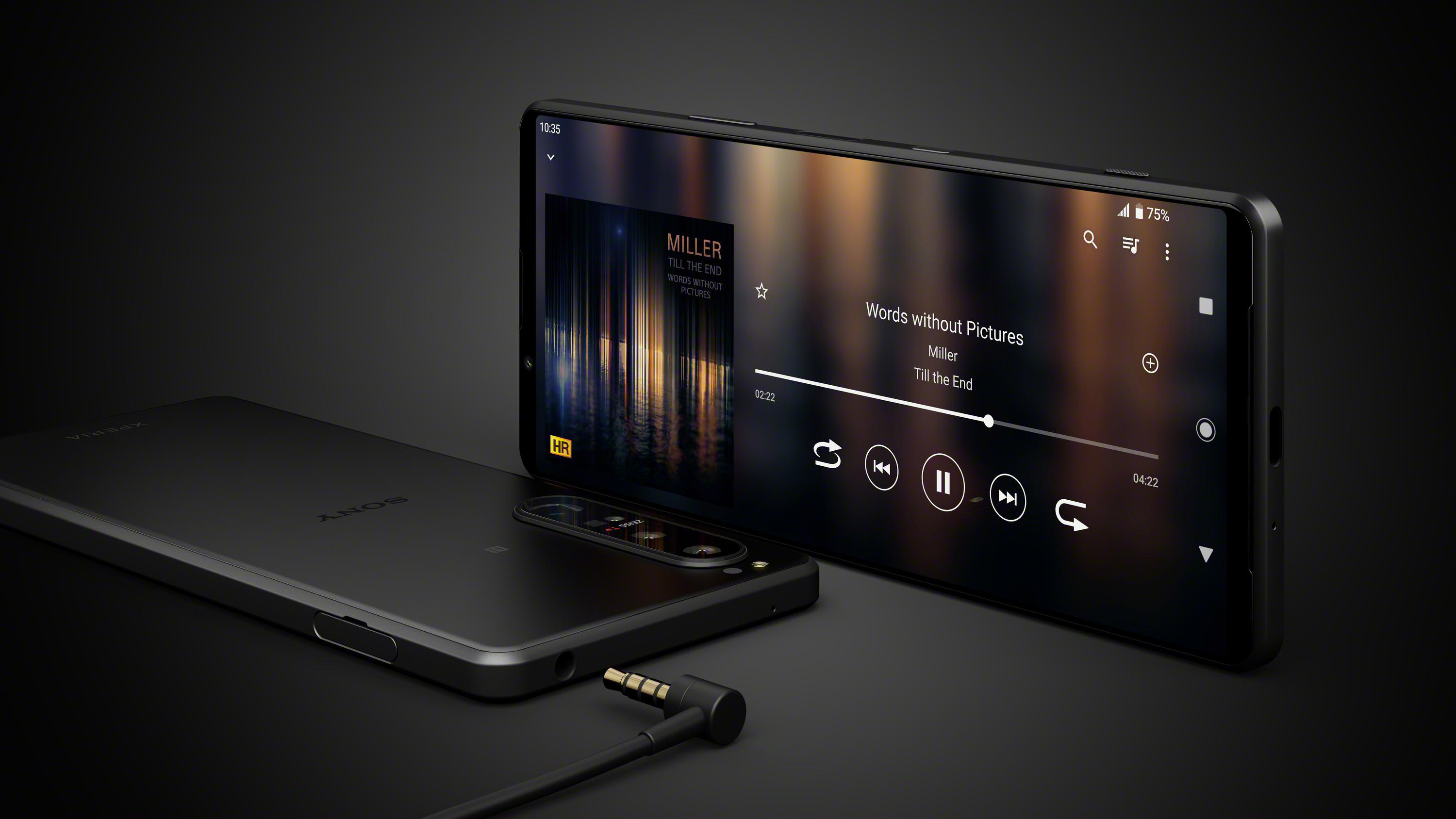 Schwarzes Smartphone mit Musikoberfläche auf dem Bildschirm und Kopfhöreranschluss. Dunkler Hintergrund.