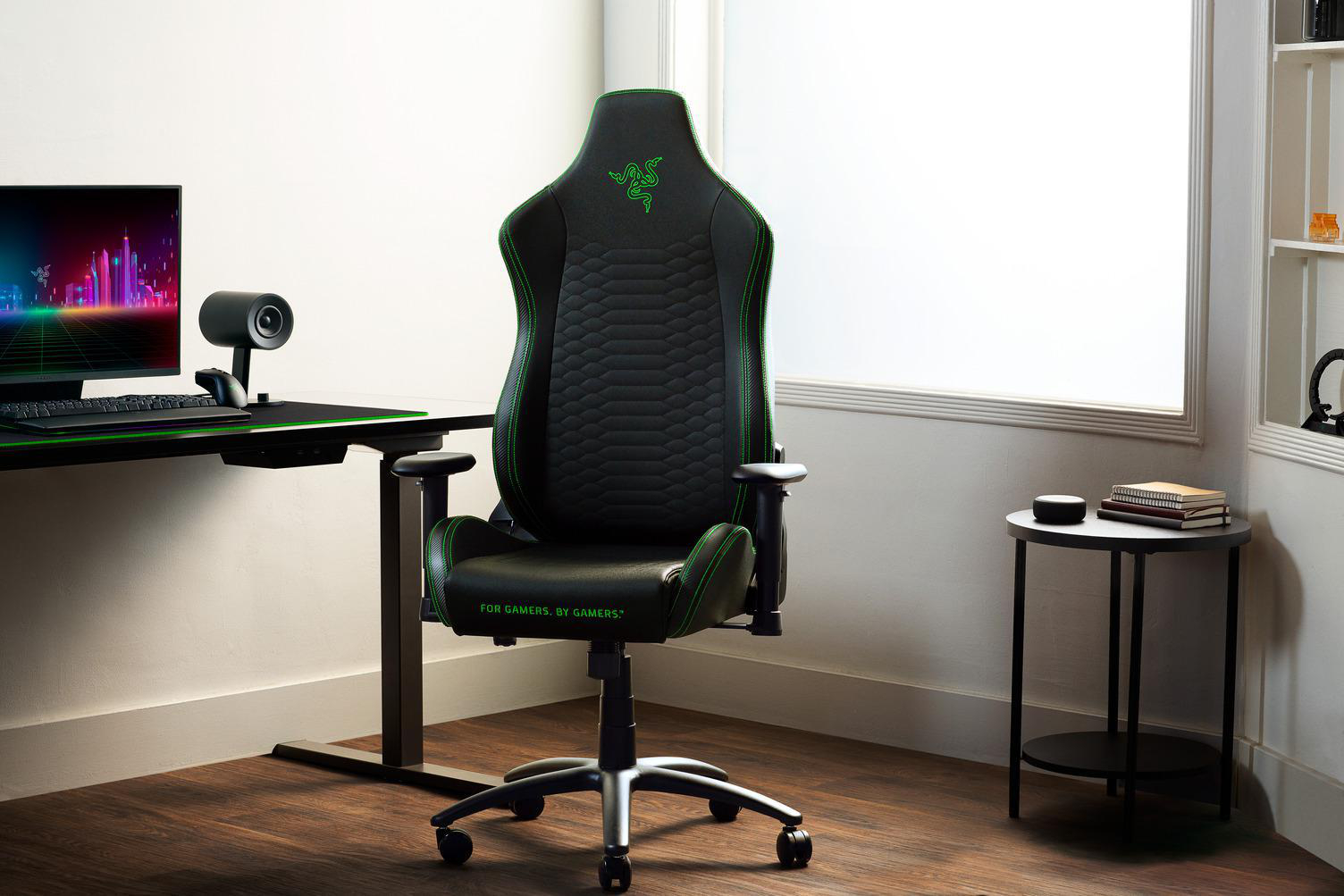 Schwarzer Gaming-Stuhl mit grünen Akzenten. Ein Schreibtisch und Monitor dahinter.