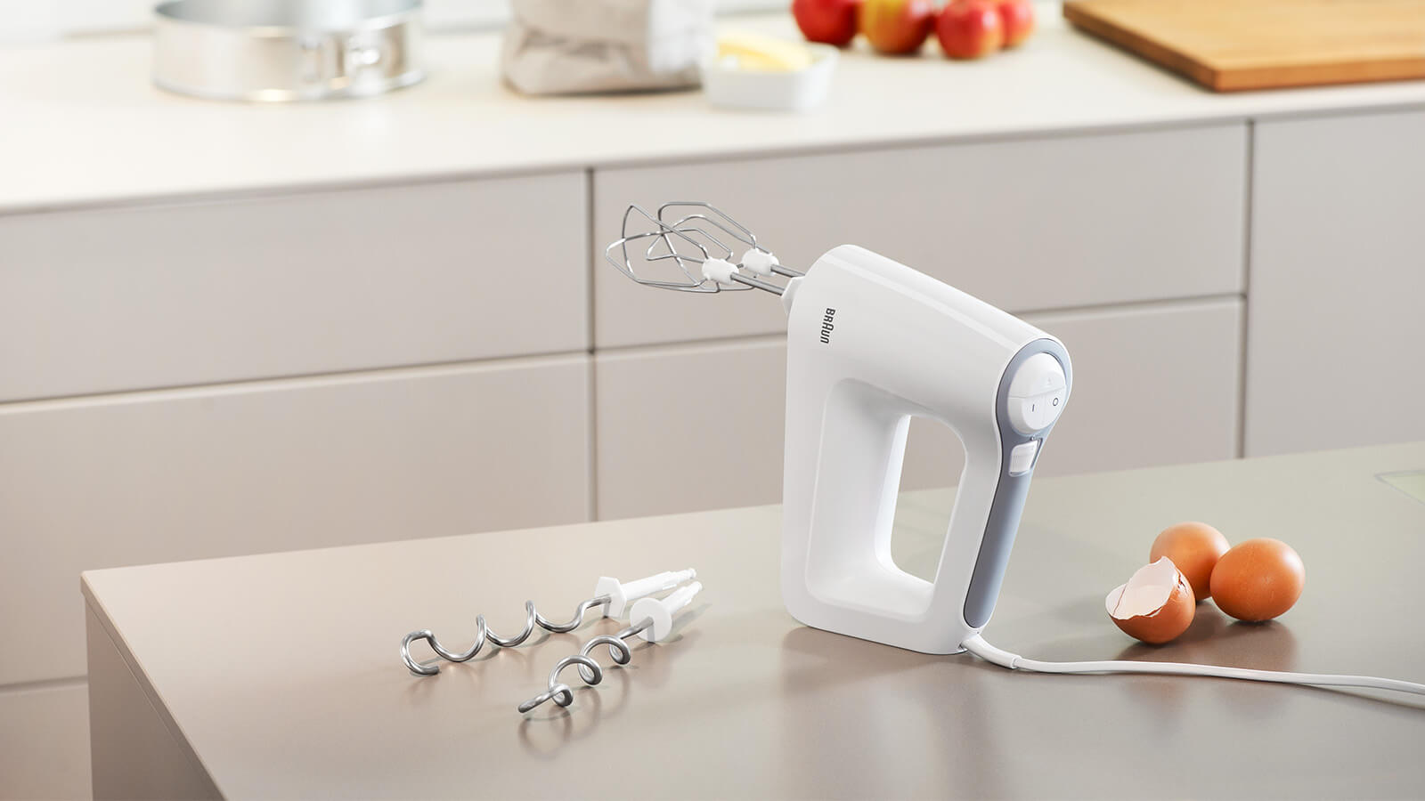 Witte handmixer op een aanrecht met eieren en opzetstukken.