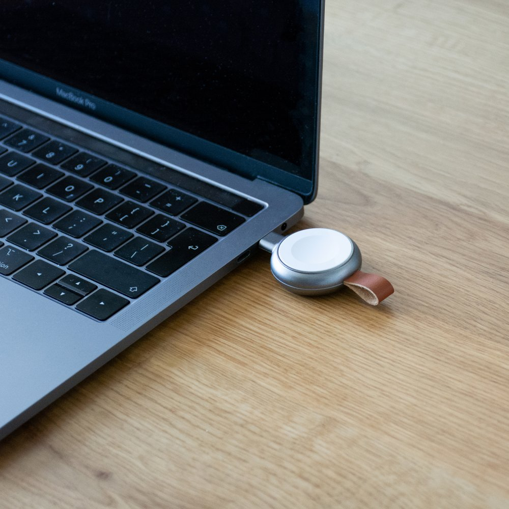 Ein silbernes Apple Watch-Ladegerät ist an ein MacBook Pro angeschlossen.