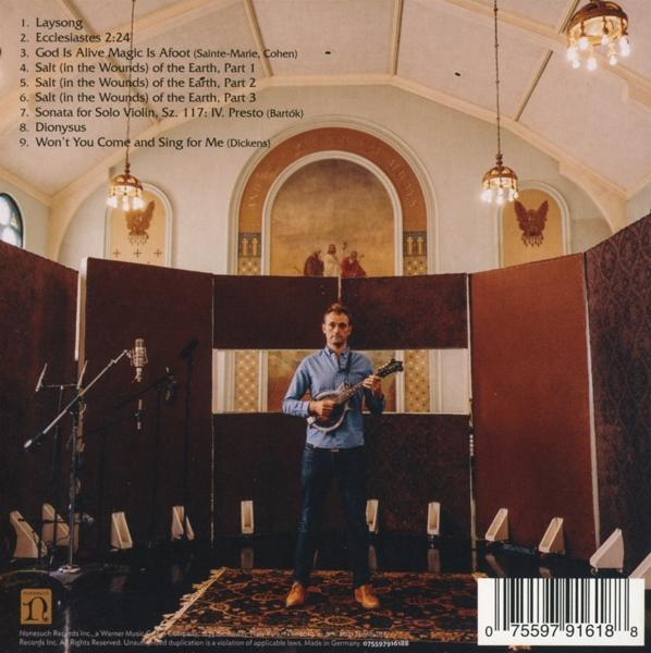 Ein Mann mit einer Mandoline steht auf einer Bühne mit einer Kulisse, auf der Songtitel stehen.