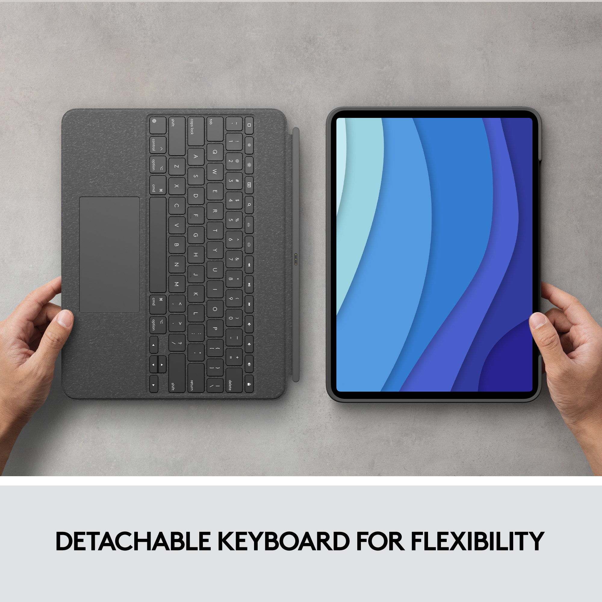 Clavier détachable et tablette. Mains tenant chacun, sur une surface grise. Clavier avec pavé tactile.