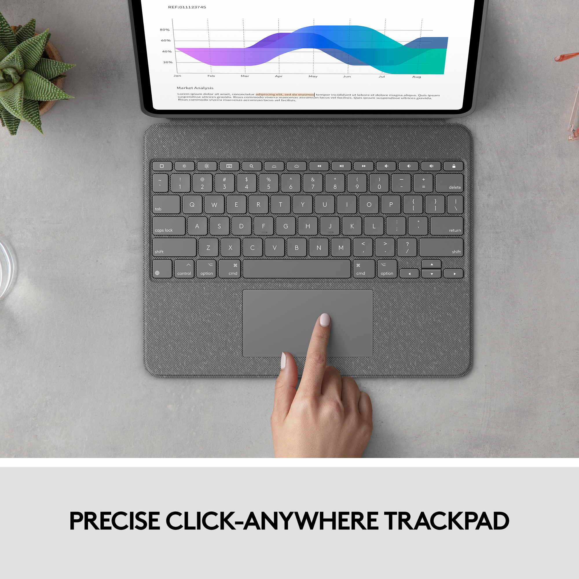 Une main sur un pavé tactile gris d'un clavier. Une tablette avec un graphique est en arrière-plan.