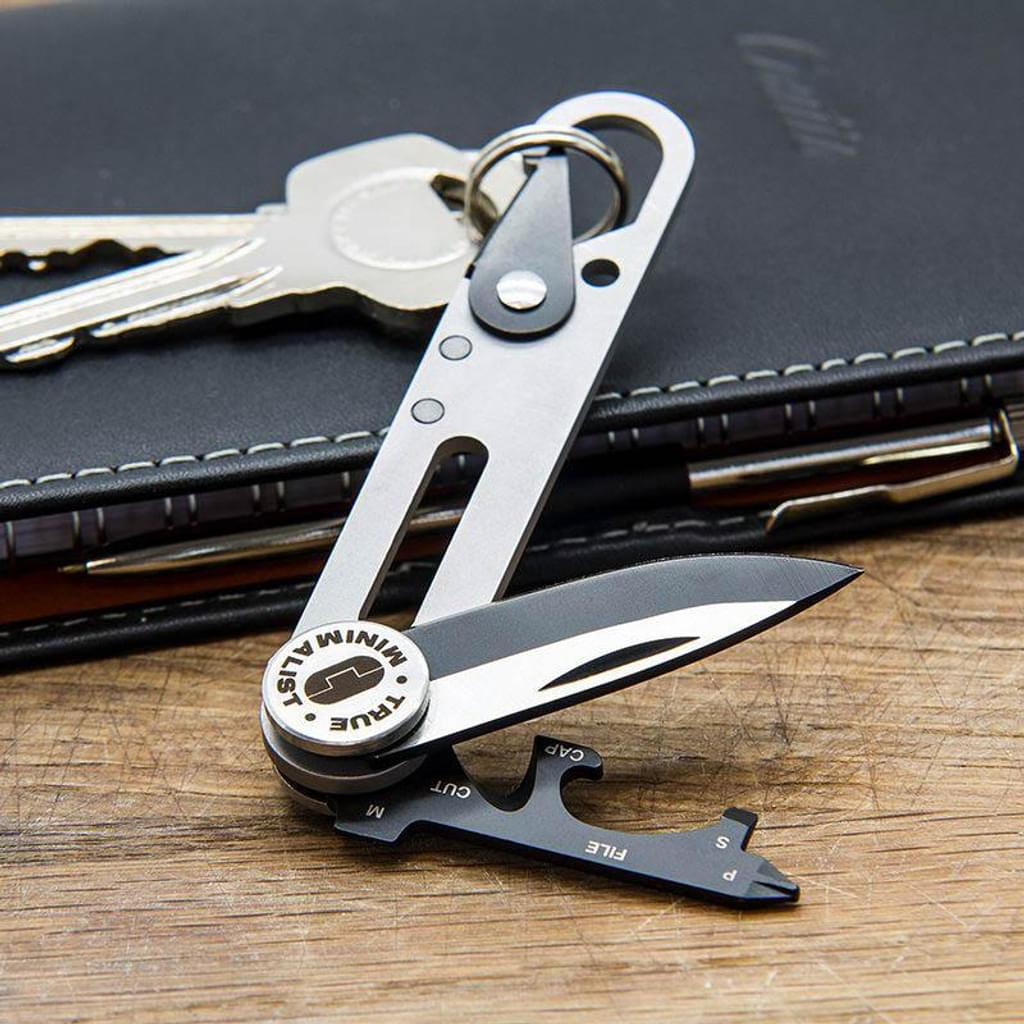 Egy kis multitool kés és kulcstartó egy fa felületen, egy pénztárca mellett.