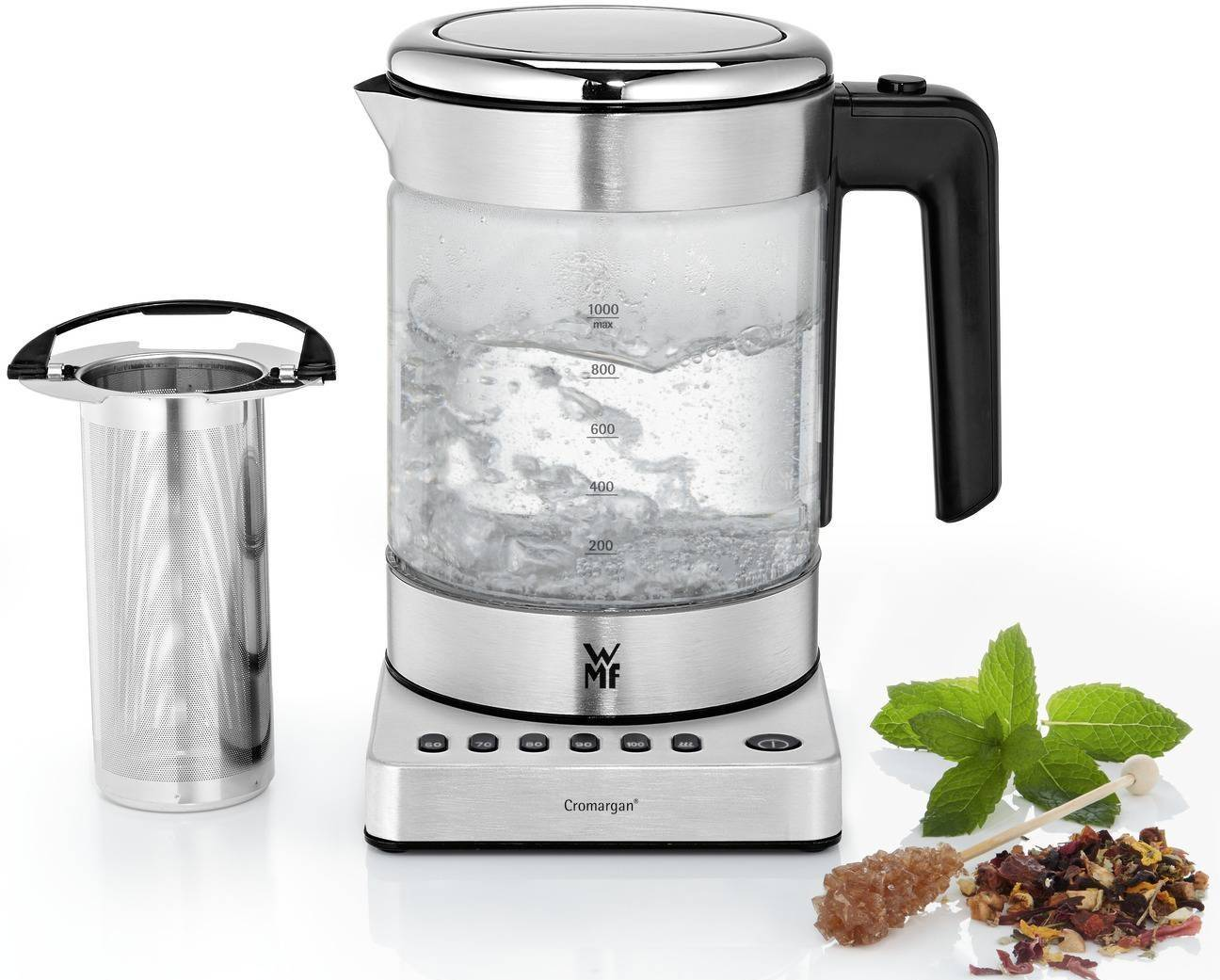 Ein Wasserkocher aus Edelstahl mit kochendem Wasser, Tee-Sieb, Minze, Zucker und Teeblättern auf weißem Untergrund.