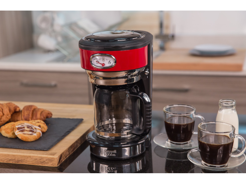 Una cafetera roja y negra con una jarra de vidrio, dos tazas de café y pasteles en una tabla.