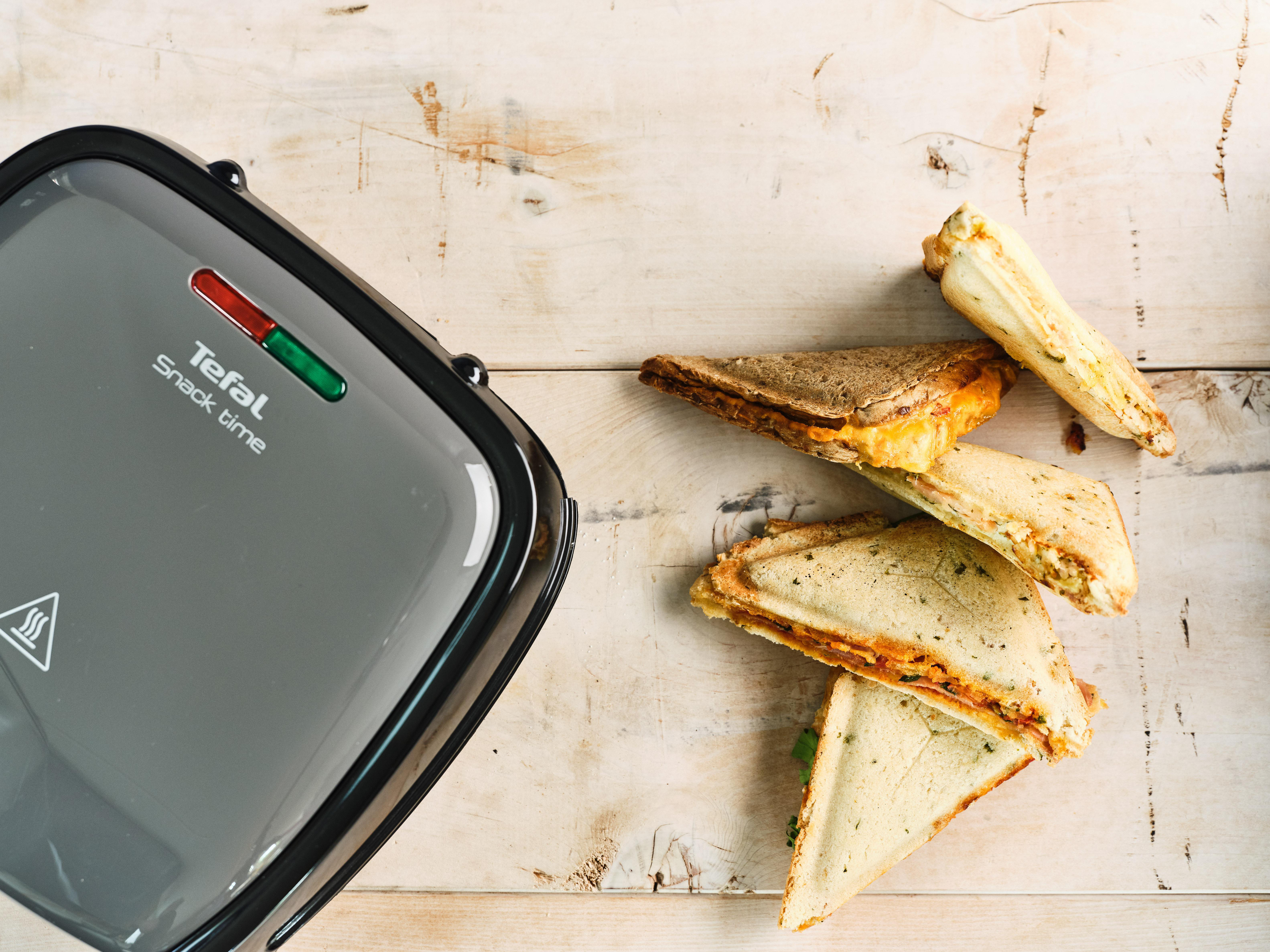 Draufsicht auf einen Sandwichmaker mit Sandwiches auf einer Holzoberfläche.