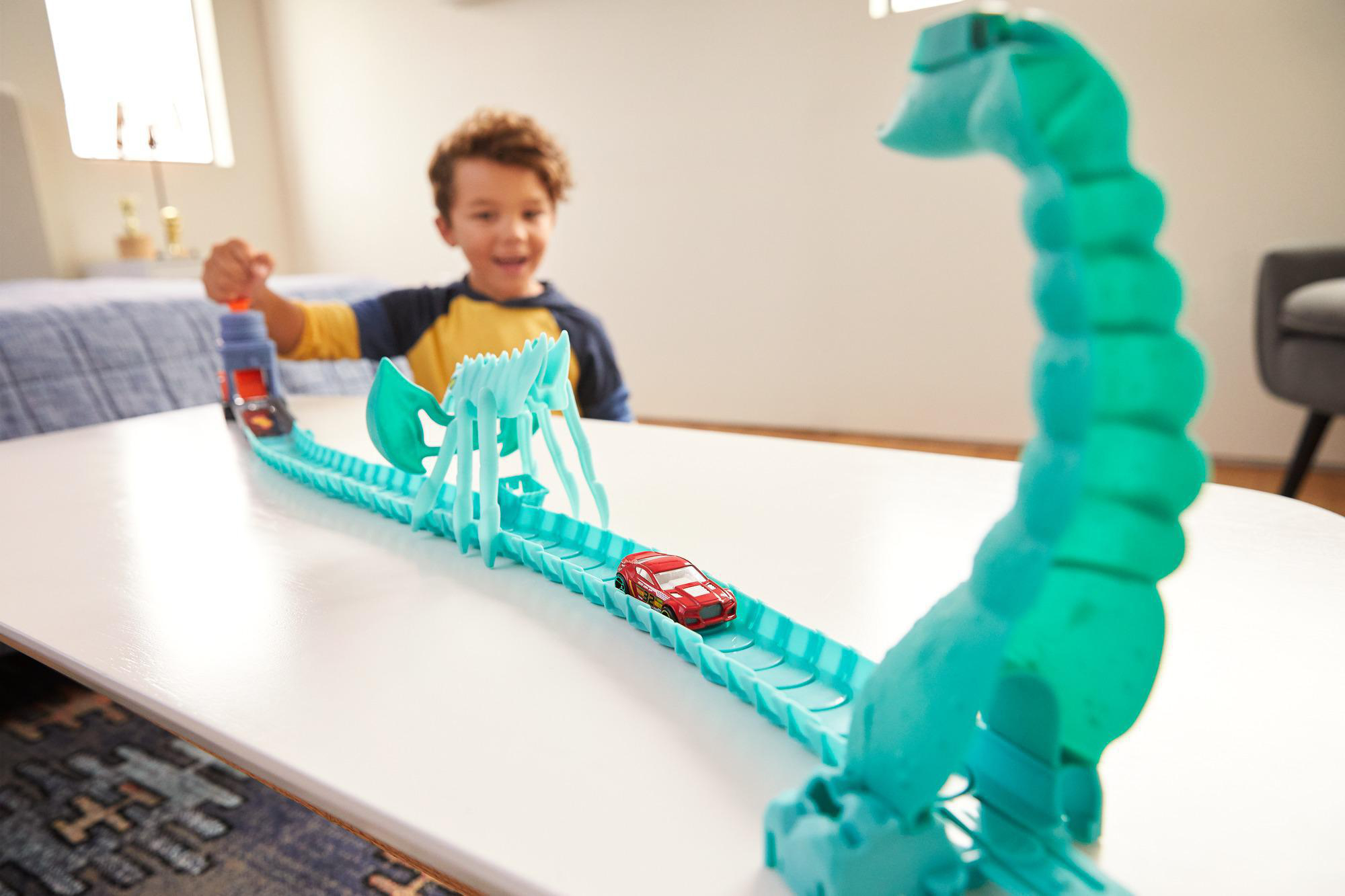 Ein Junge spielt mit einem Spielzeugauto auf einer Rennstrecke. Das rote Auto rast. Die Strecke hat einen grünen Looping und eine blaue Brücke.