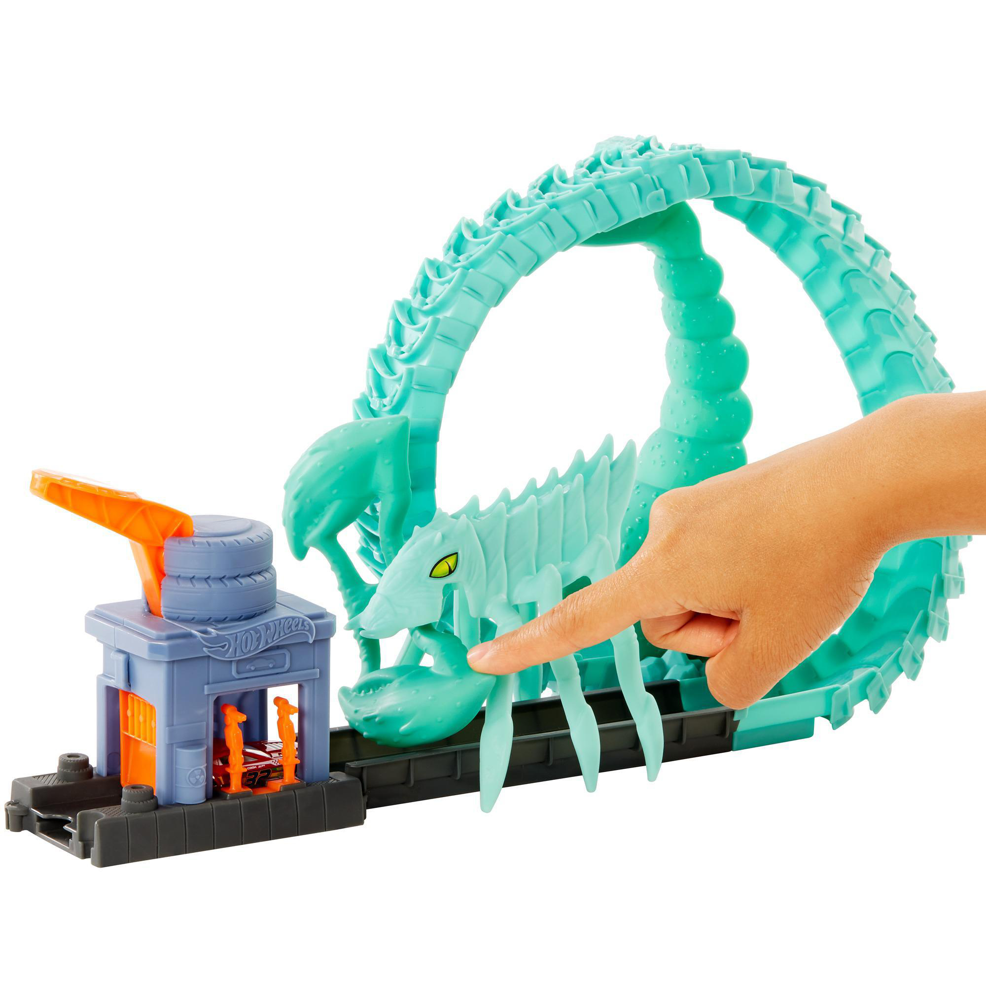 Eine Hot Wheels-Strecke mit einem Skorpionbogen. Eine Hand zeigt darauf. Ein Auto befindet sich in einer Garage.