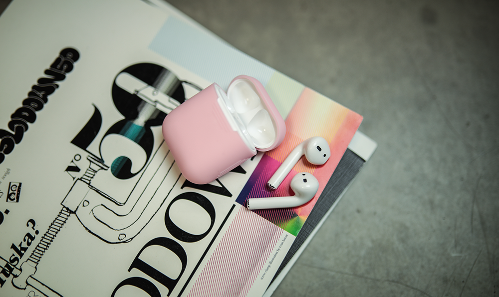 White AirPods and case on a colorful magazine. Case is pink.