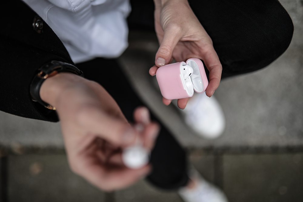 Woman holding a pink AirPods case with white AirPods inside. A single AirPod is held separately.