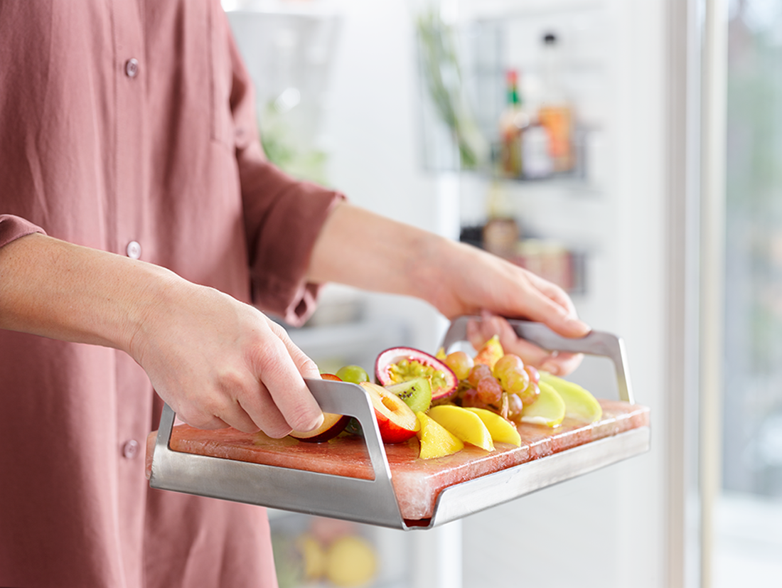 Person holding a tray of fruits: grapes, passion fruit, mango, and peach. Pink stone tray.