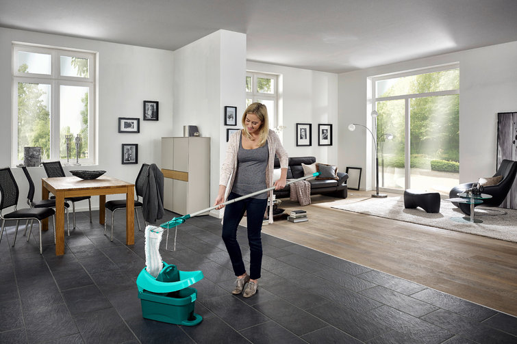 Frau, die ein Zimmer wischt. Sie steht in der Mitte mit einem Wischmopp und einem Eimer.
