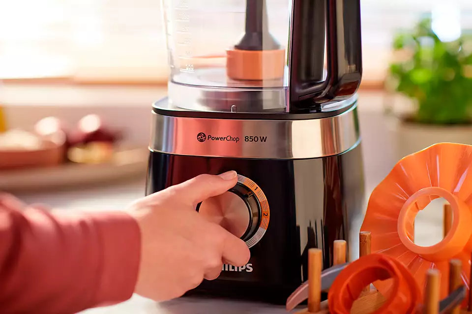 Egy személy keze a Philips konyhai robotgépén a tárcsát forgatja, narancssárga kiegészítőkkel.