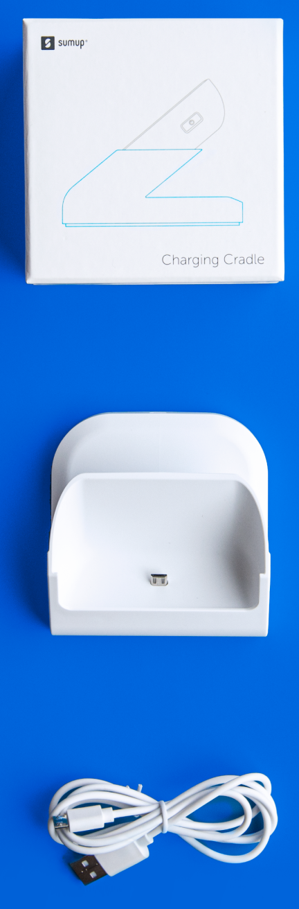 A white charging cradle with a USB cable and a white box with the sumup logo and charging cradle outline.