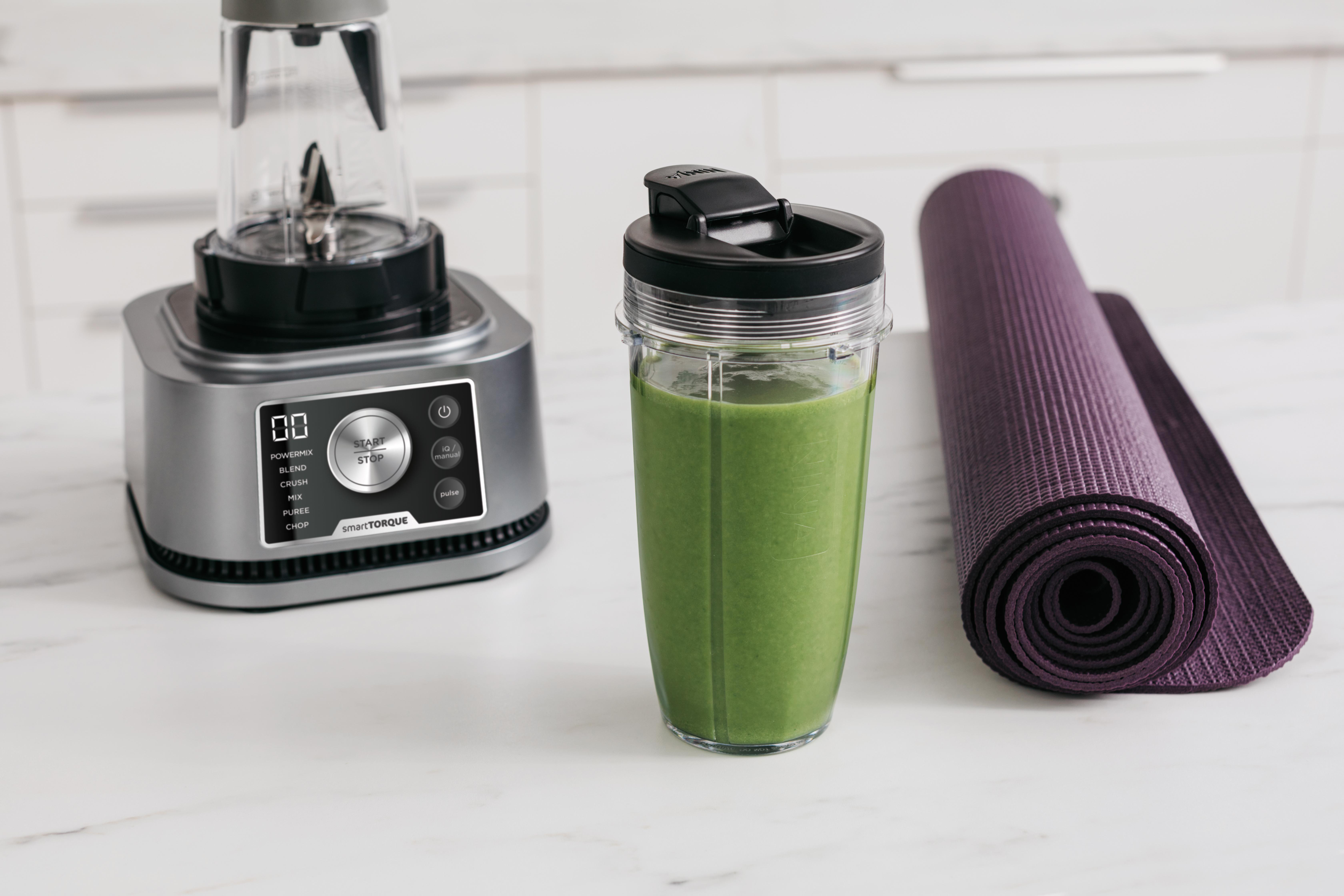 Ein Mixer mit grünem Smoothie, eine Yogamatte und ein weißer Küchenhintergrund.