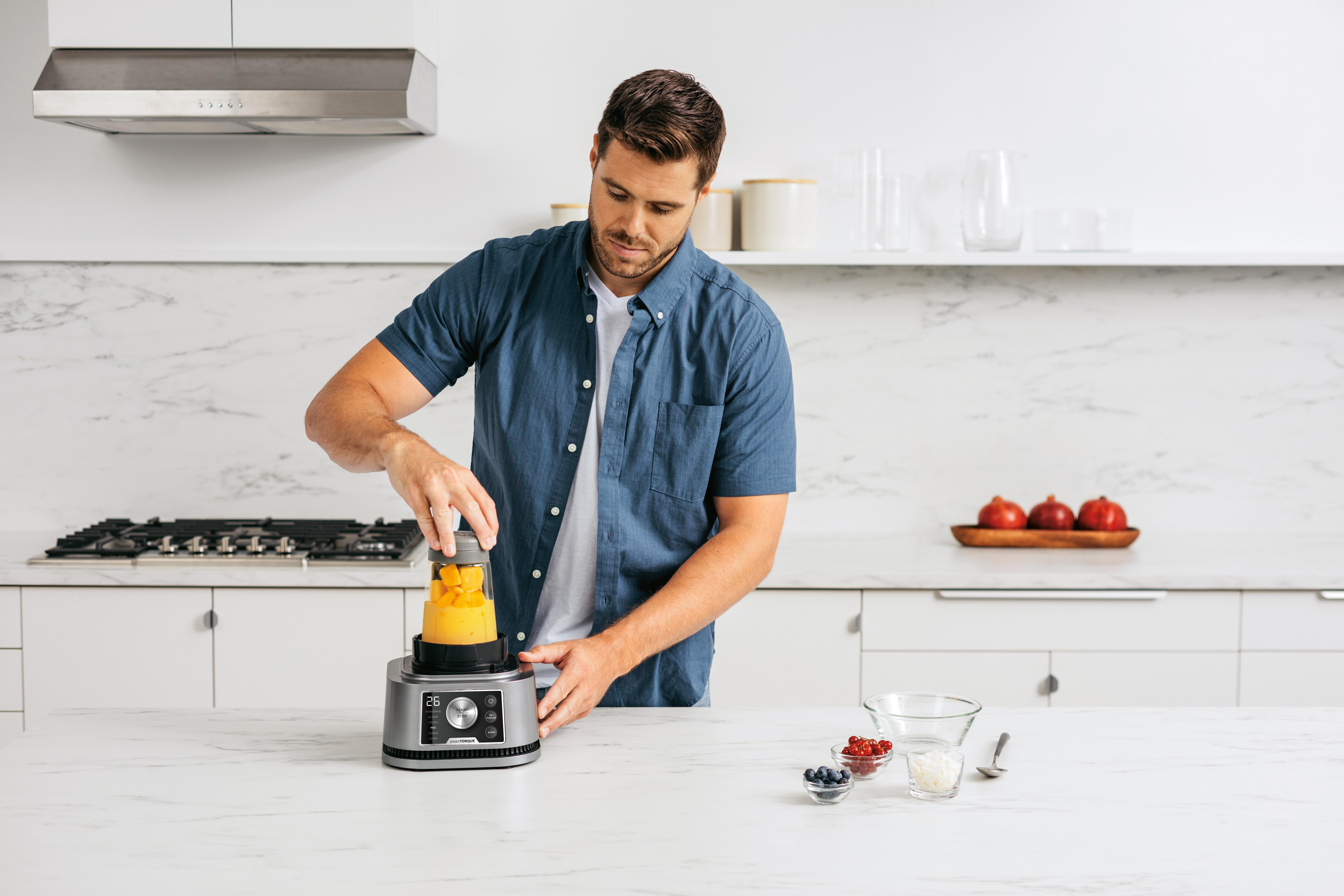 Mann bereitet Smoothie im Mixer zu, mit Früchten auf der Arbeitsplatte.