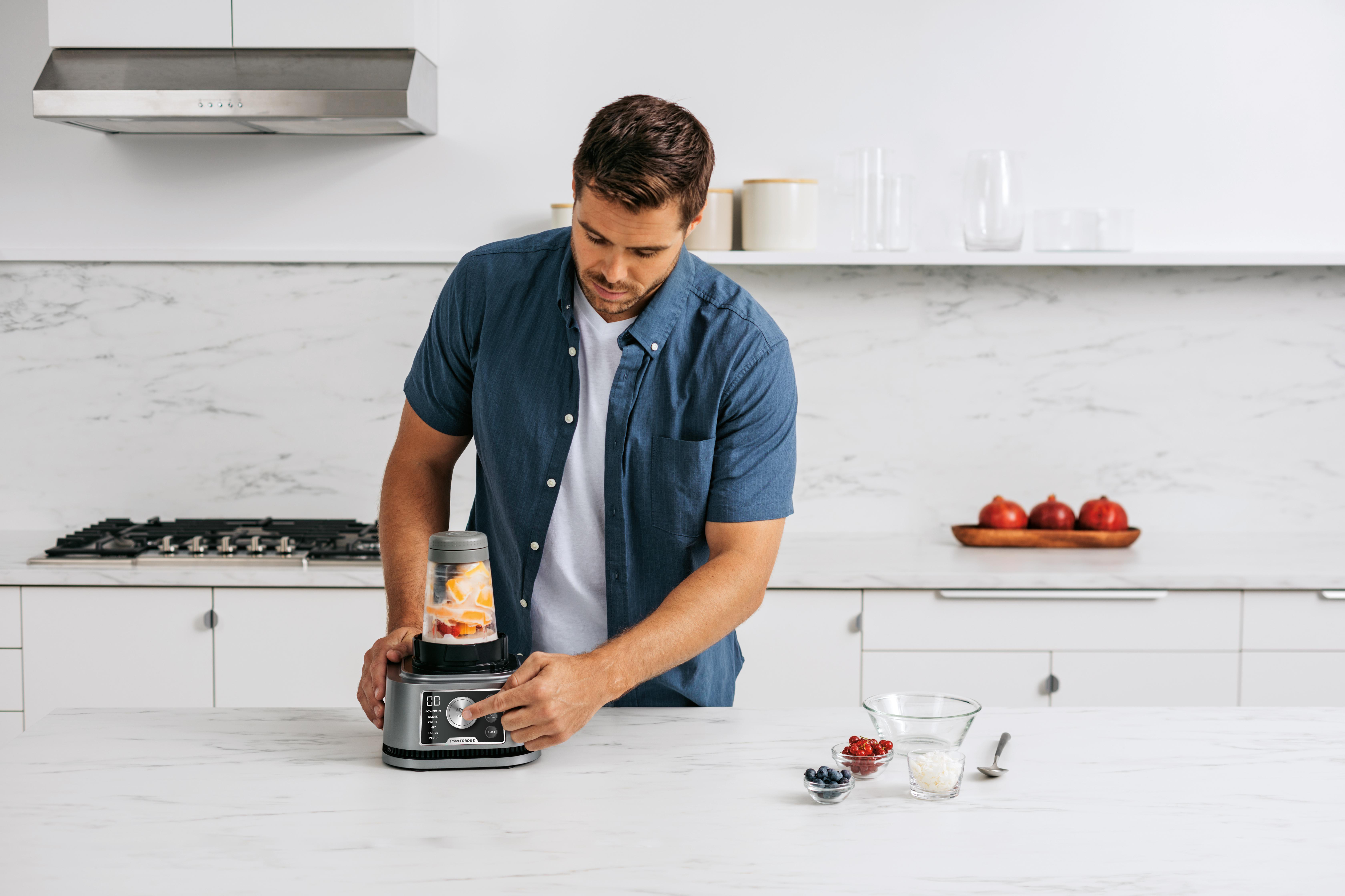 Ein Mann benutzt einen Mixer mit Obst und Zutaten auf einer Arbeitsplatte.