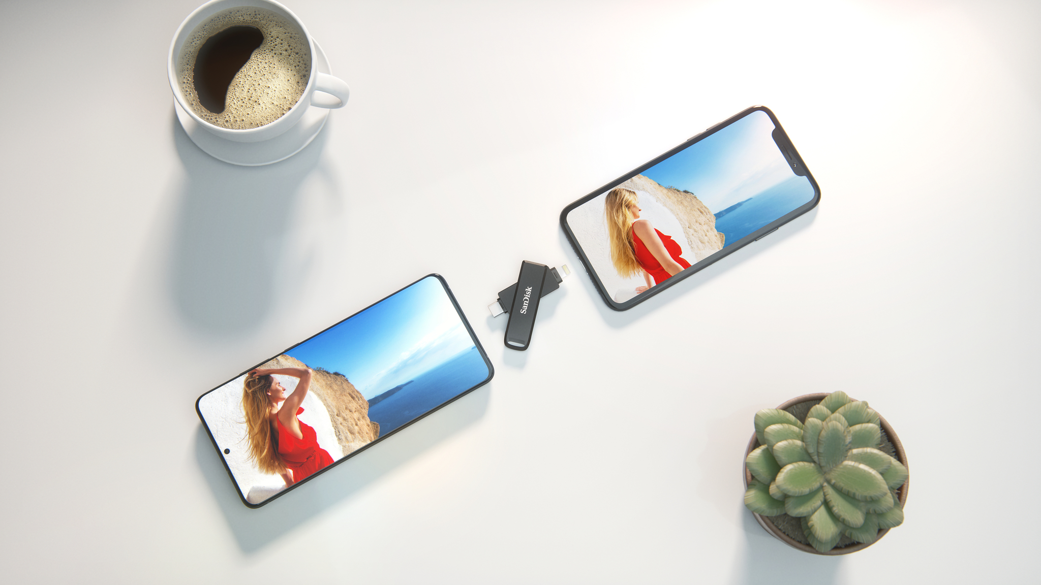Két telefon és egy USB-meghajtó fehér felületen, kávéscsésze és növény.