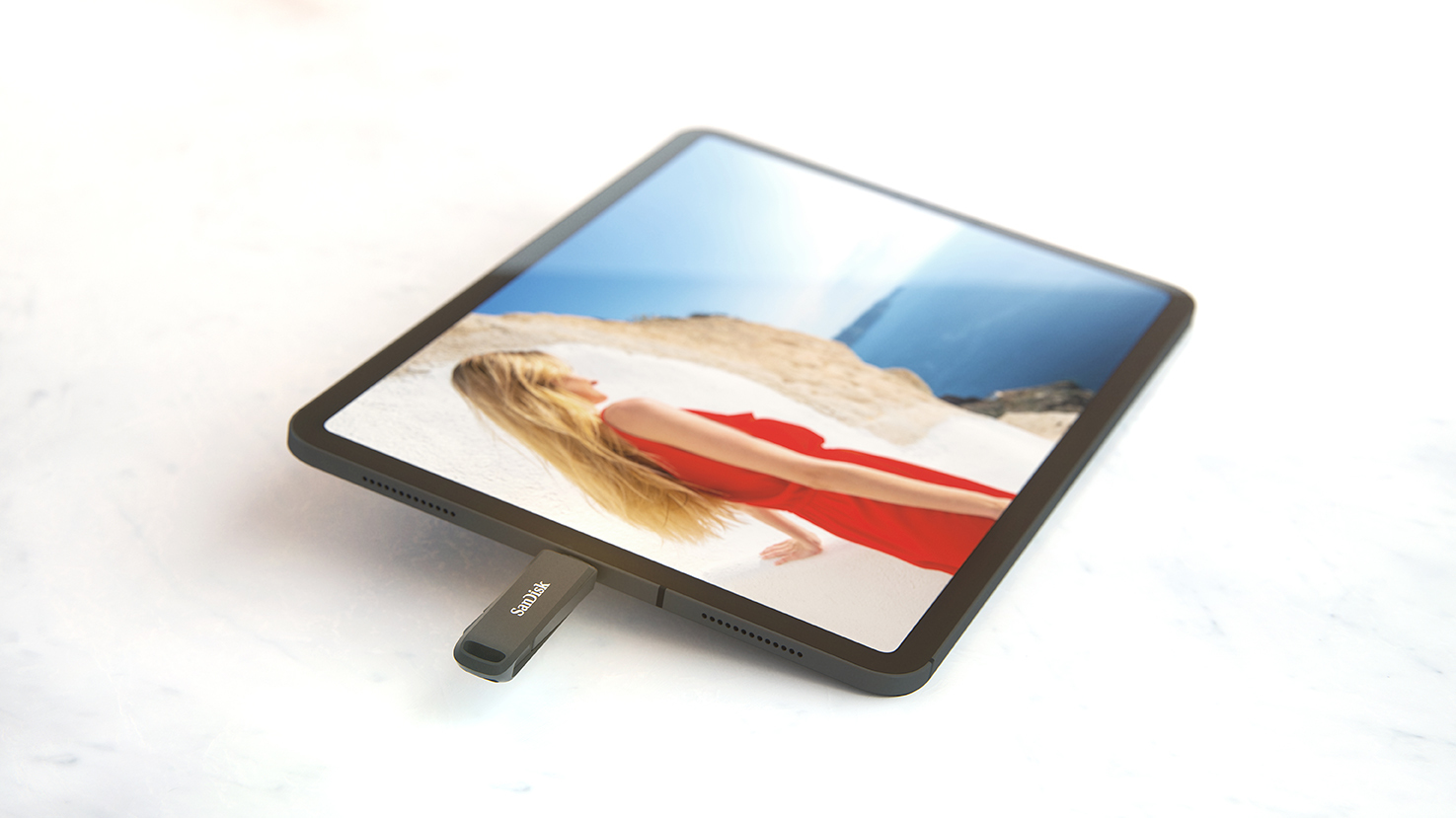 Fekete táblagép, USB meghajtóval. A képernyő egy piros ruhás nőt mutat.