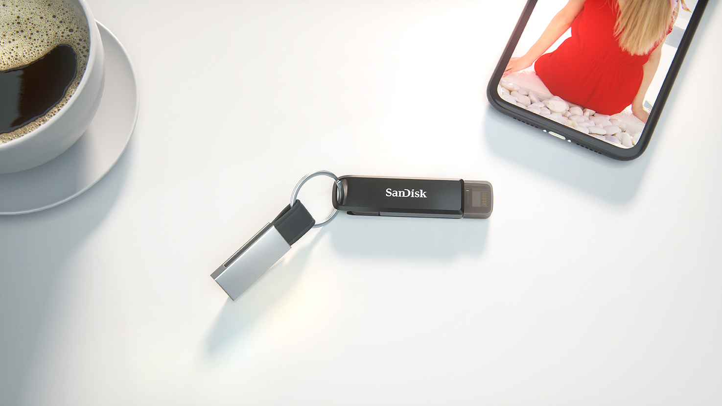 USB meghajtó kulcstartón egy piros ruhás nőt mutató telefon mellett.
