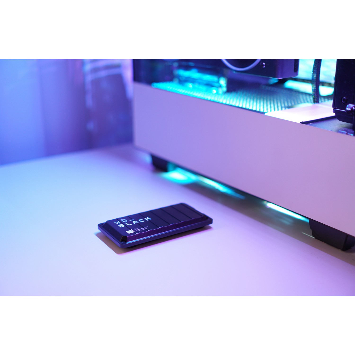 Disco duro externo WD_BLACK negro sobre una superficie clara, con una computadora al fondo.