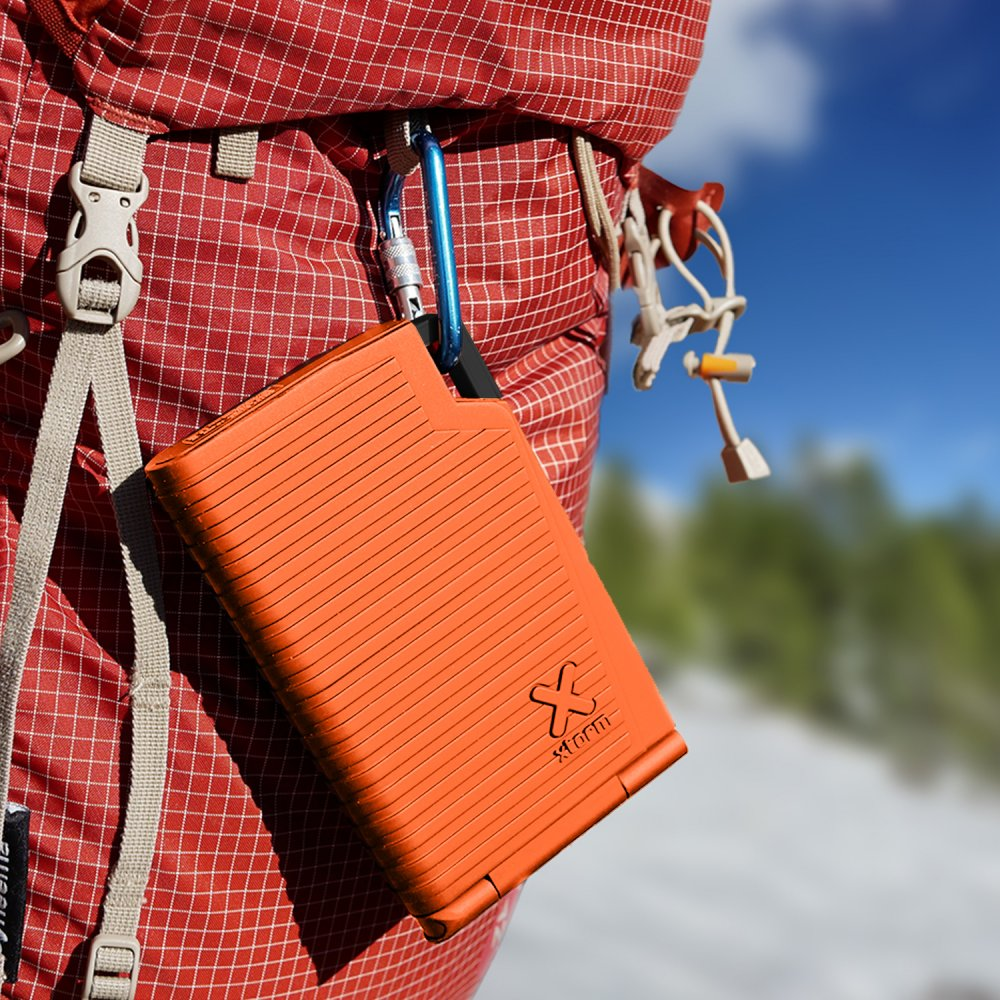 Ein oranges, rechteckiges Speichergerät wird mit einem blauen Karabiner an einem Rucksack befestigt.