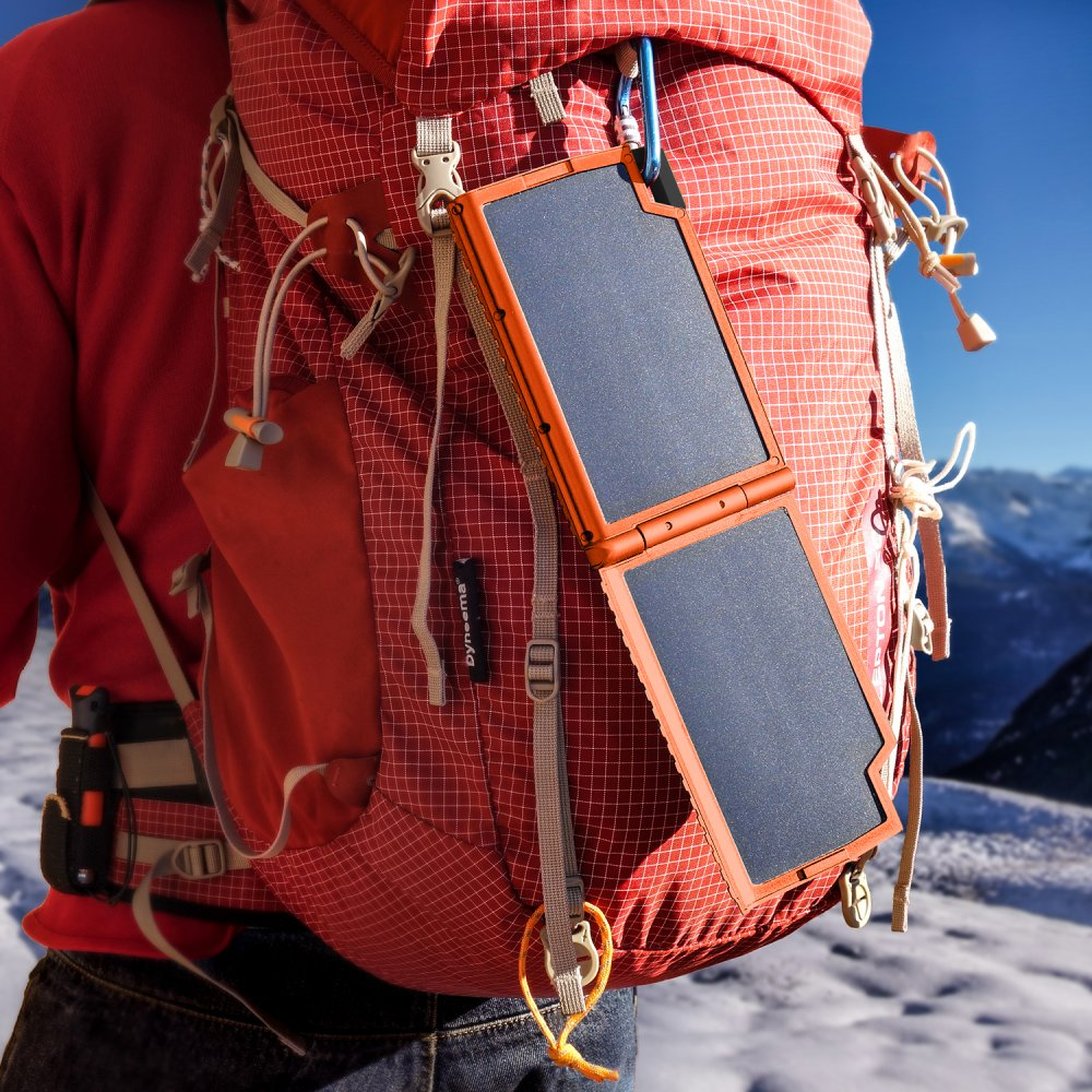 Rucksack mit Solarpanel, das ein Gerät auflädt, in einer verschneiten Landschaft.