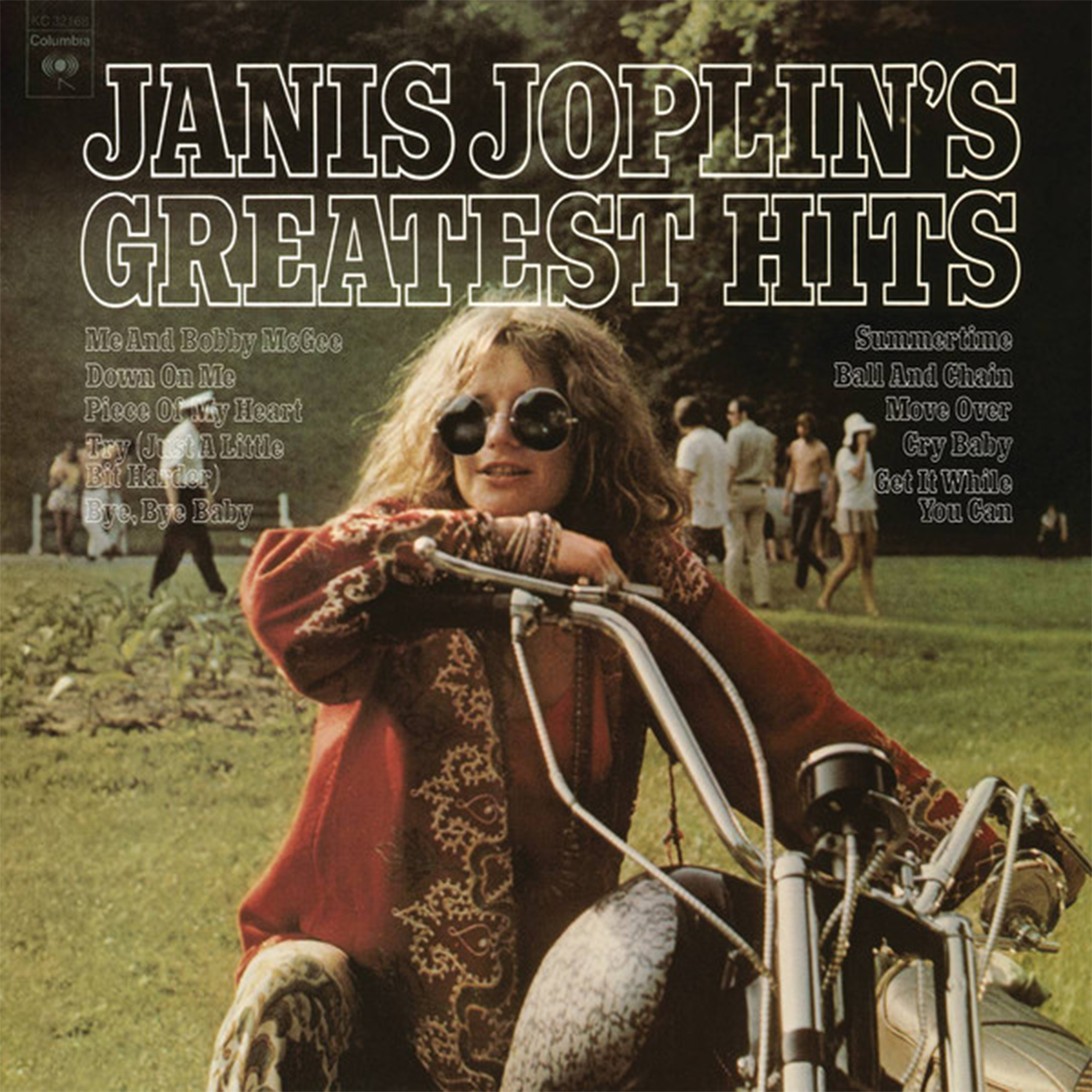 Janis Joplin seduta su una moto, con occhiali da sole e top fantasia.