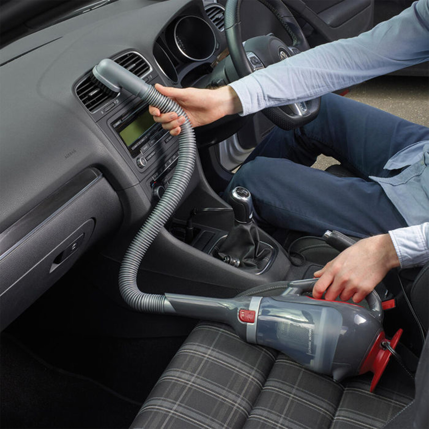Una persona usa un aspirapolvere portatile all'interno di un'auto, pulendo i sedili.
