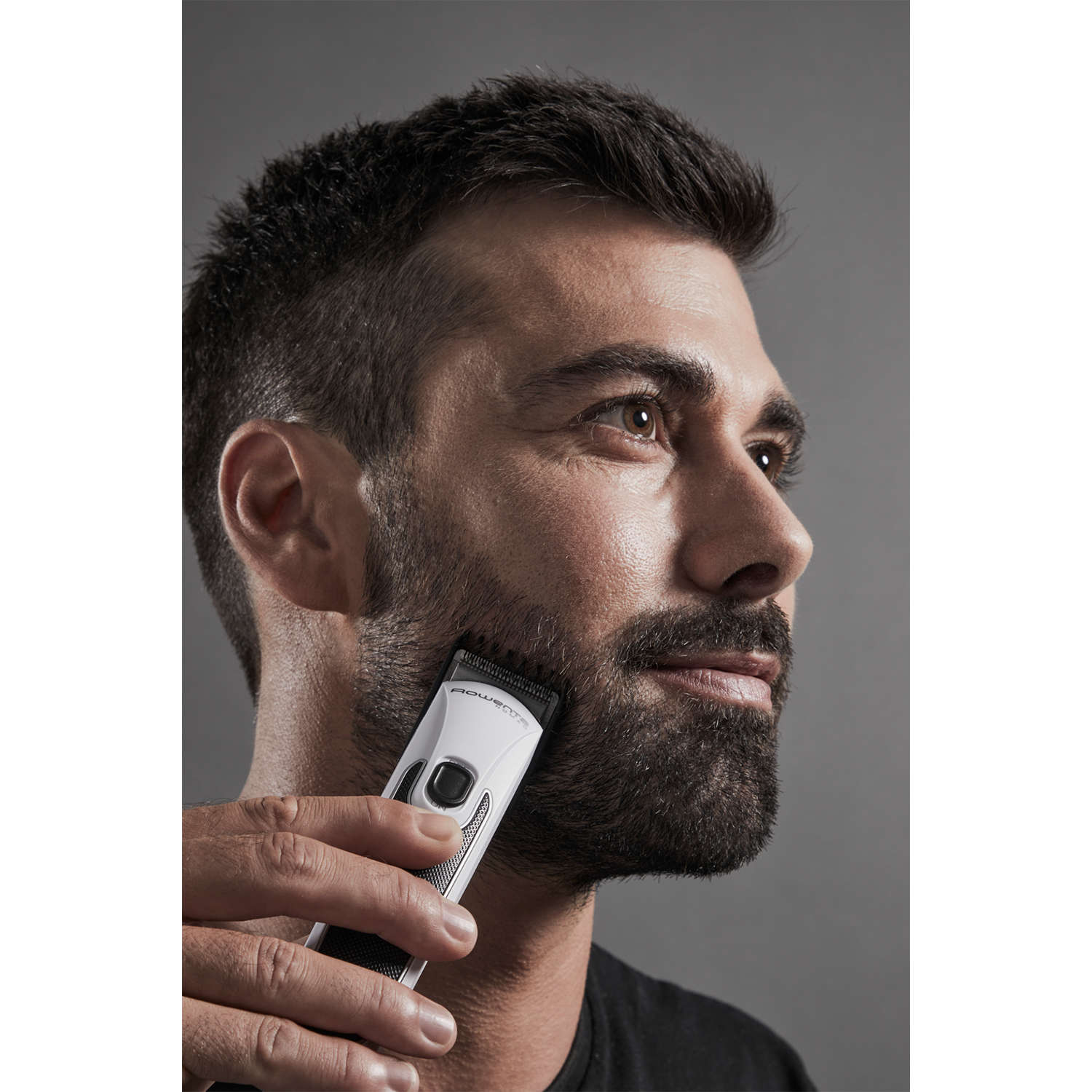 Un uomo che taglia la barba con un tagliacapelli elettrico, rivolto verso la fotocamera.