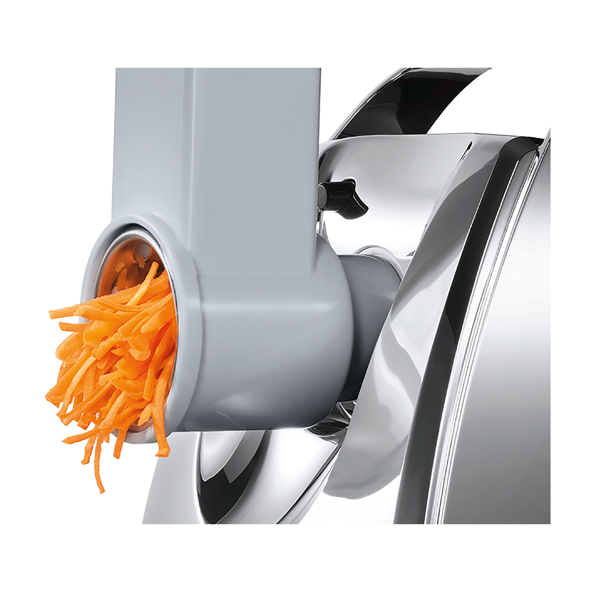 Primo piano di un robot da cucina che grattugia carote. La macchina è grigia e le carote sono arancioni.