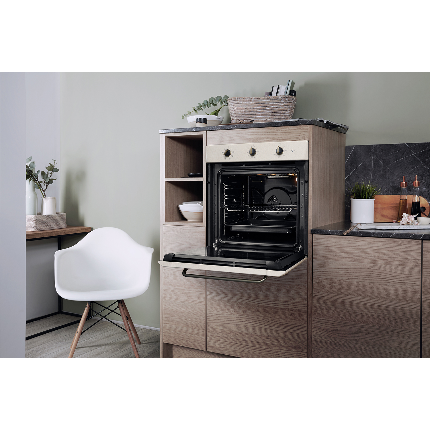 Interno cucina. Forno con porta aperta, mobili in legno, sedia bianca, parete verde.