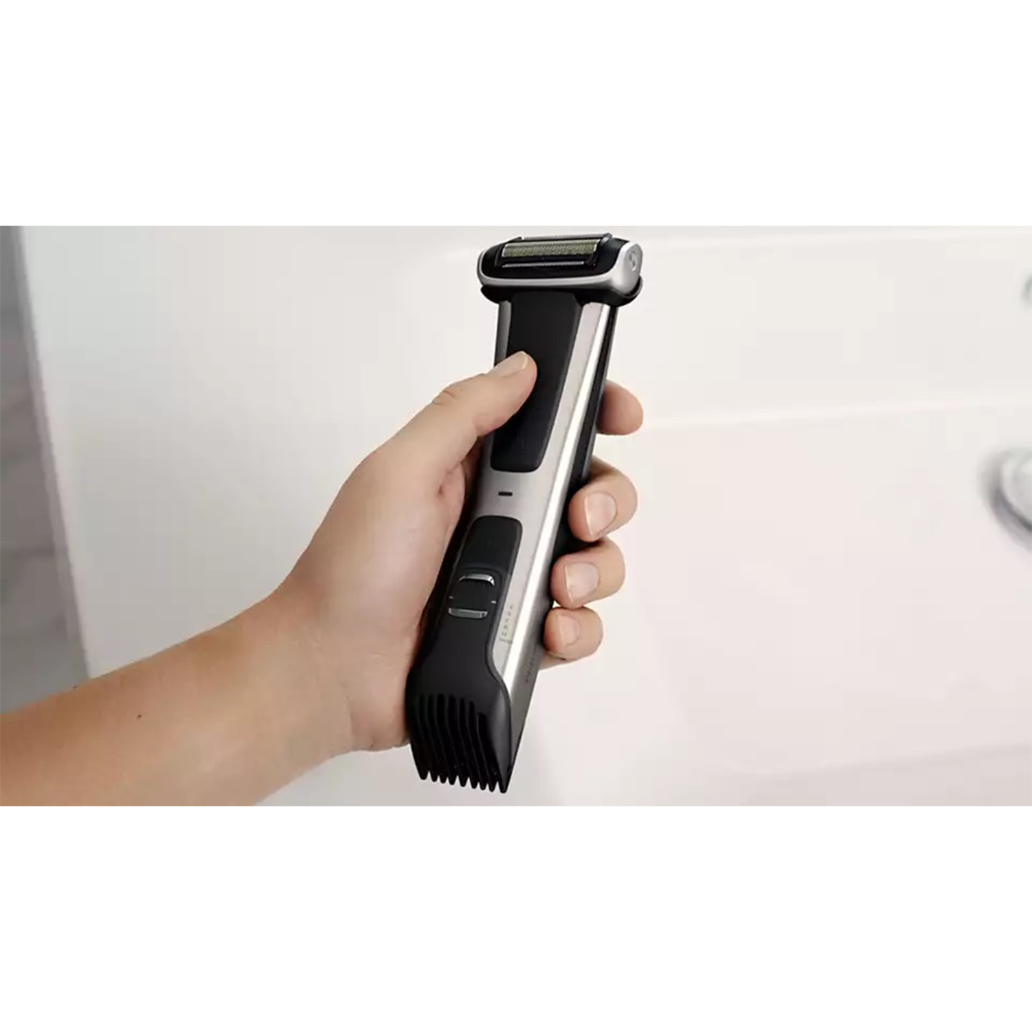 Una persona che tiene un trimmer elettrico nero e argento davanti a un lavandino bianco.