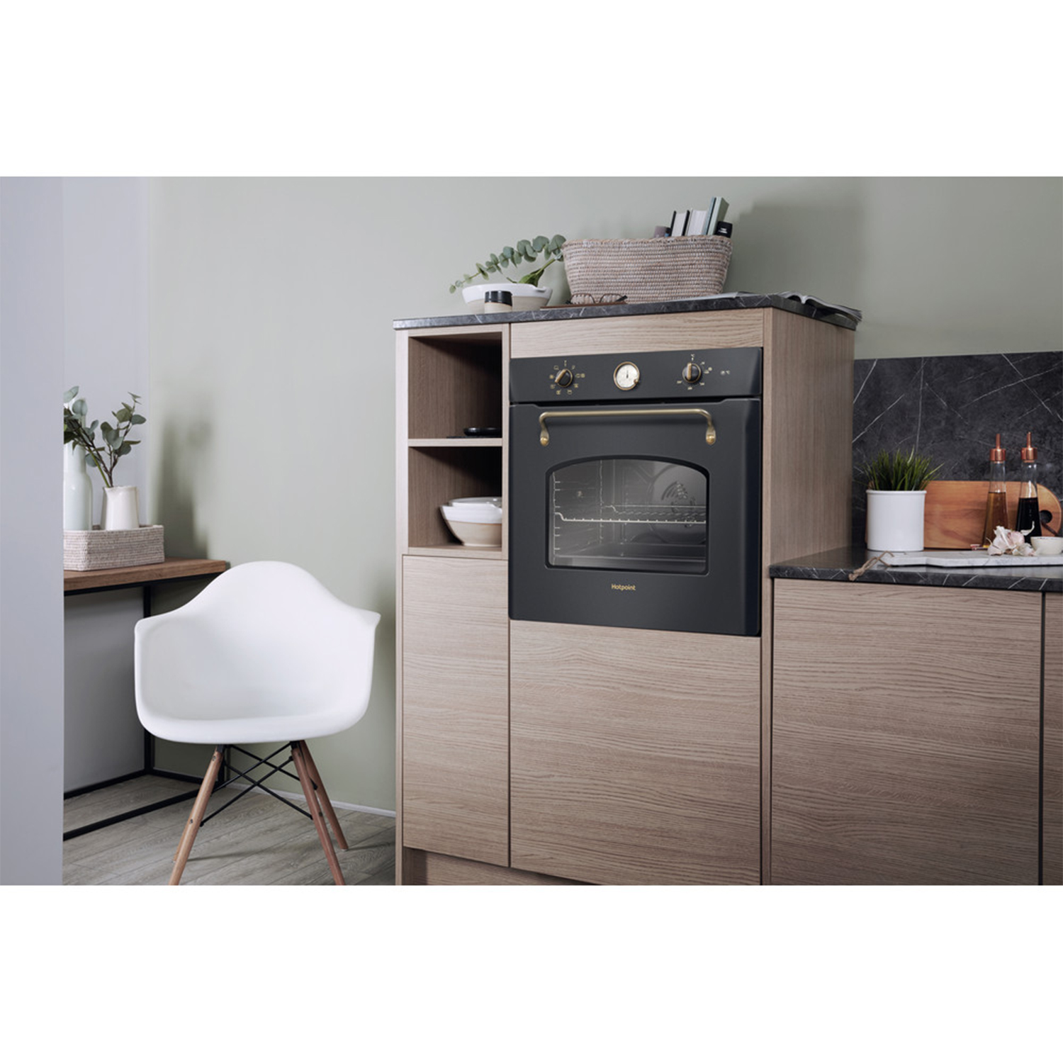 Scena di cucina con un forno nero integrato in un mobile di legno. Sono visibili una sedia bianca e delle piante.