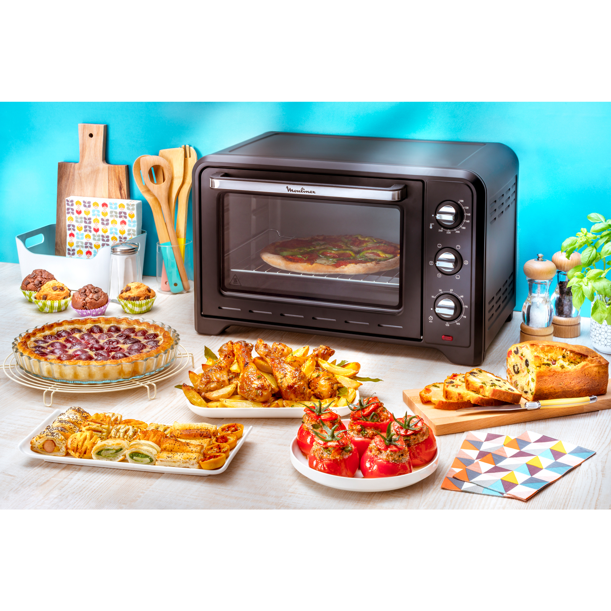 Forno pieno di pizza, circondato da vari cibi cotti su un tavolo con sfondo colorato.