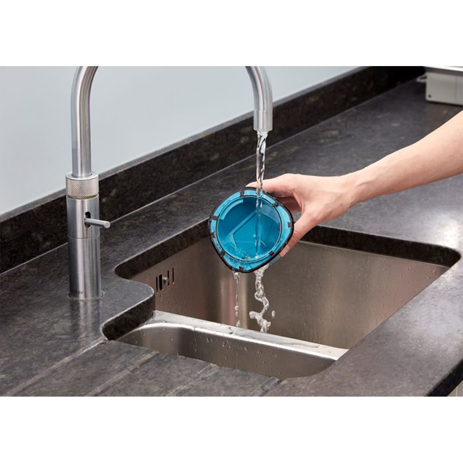 Una mano lava un filtro blu sotto un rubinetto della cucina in un lavello in acciaio inox.