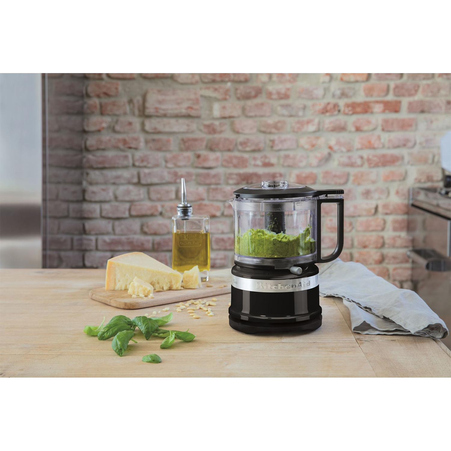 Robot da cucina nero con pesto. Formaggio, olio e basilico su tavolo legno.