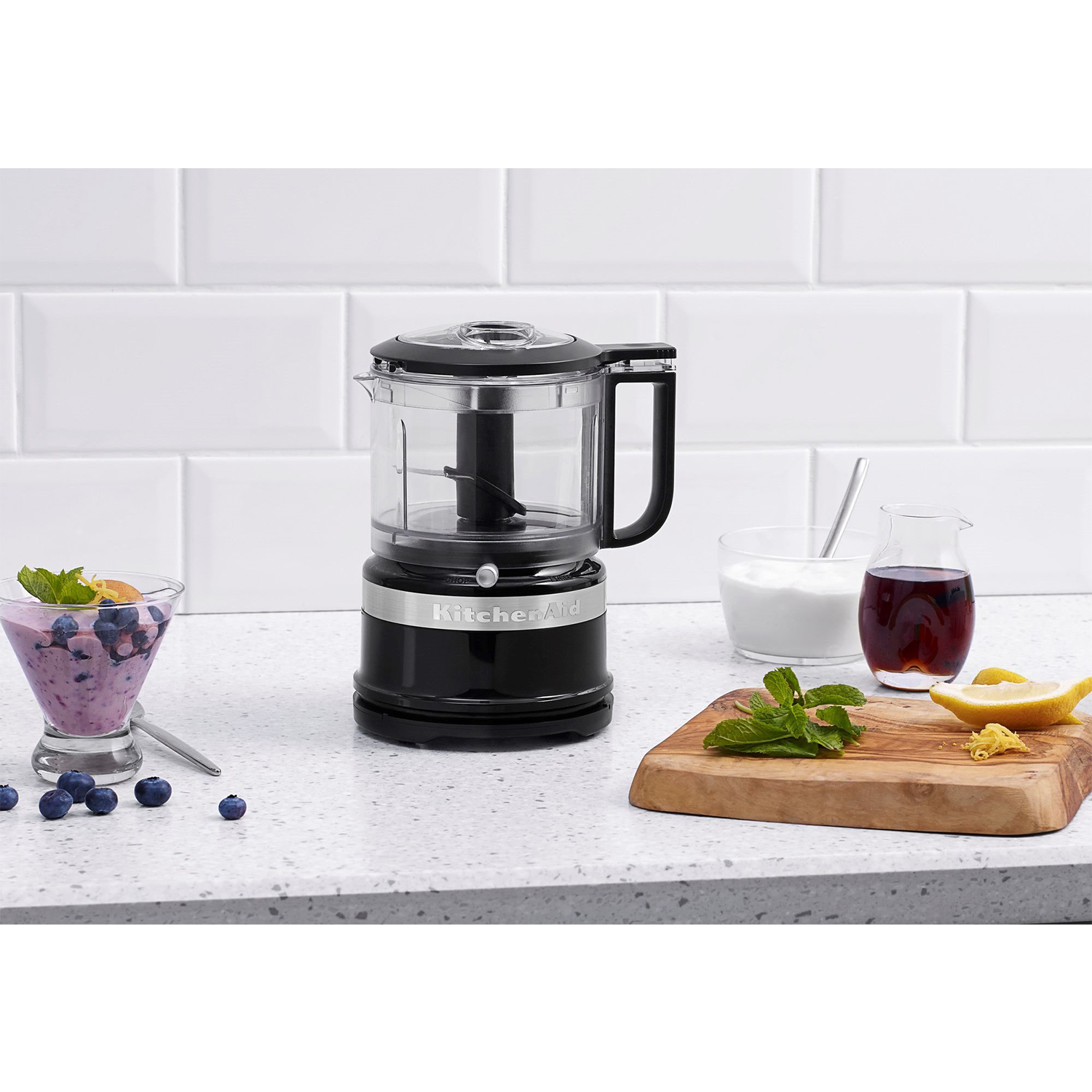 Un robot da cucina nero con ingredienti e un tagliere in legno su un bancone.