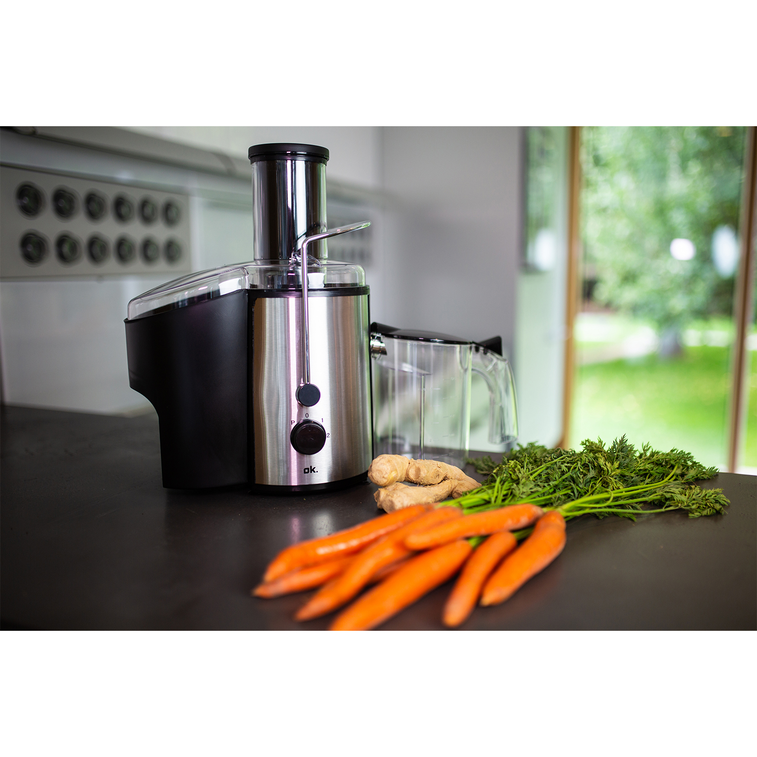 Estrattore di succo con carote, zenzero e verdure su un piano di lavoro. La cucina è lo sfondo.