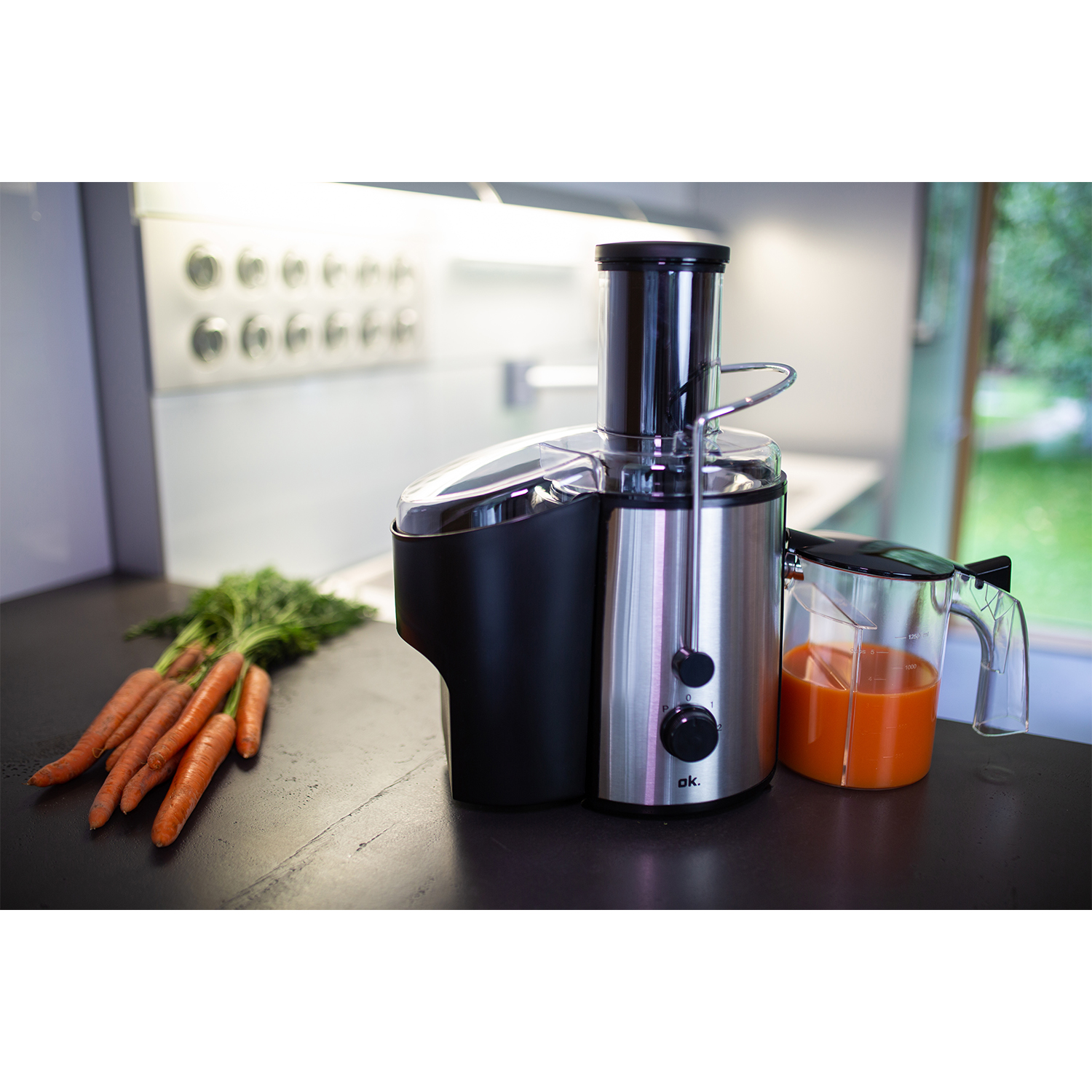 Centrifuga con carote e brocca di succo. Elettrodomestico argento e nero su superficie scura.
