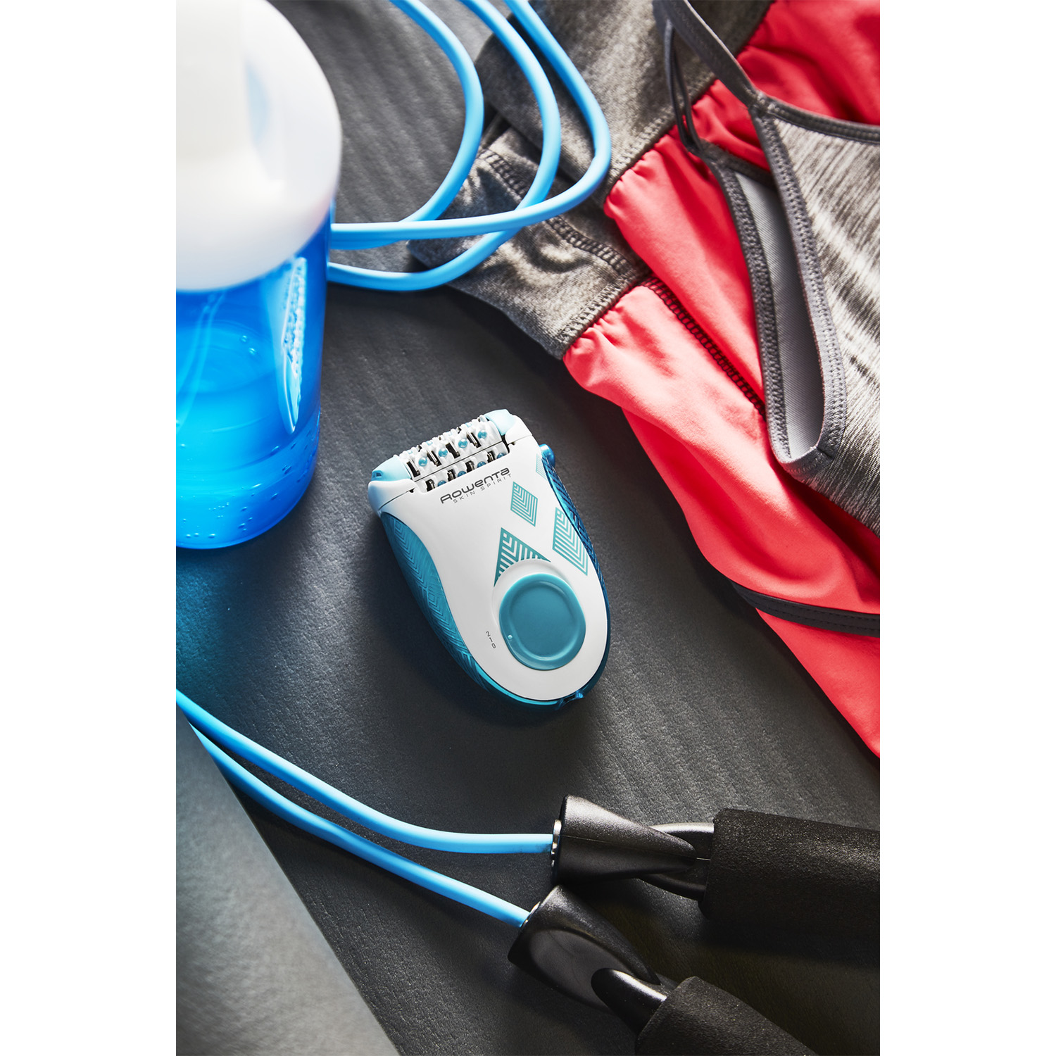 Epilatore Rowenta con parte superiore rosa e cavo blu, circondato da abbigliamento e attrezzature sportive.