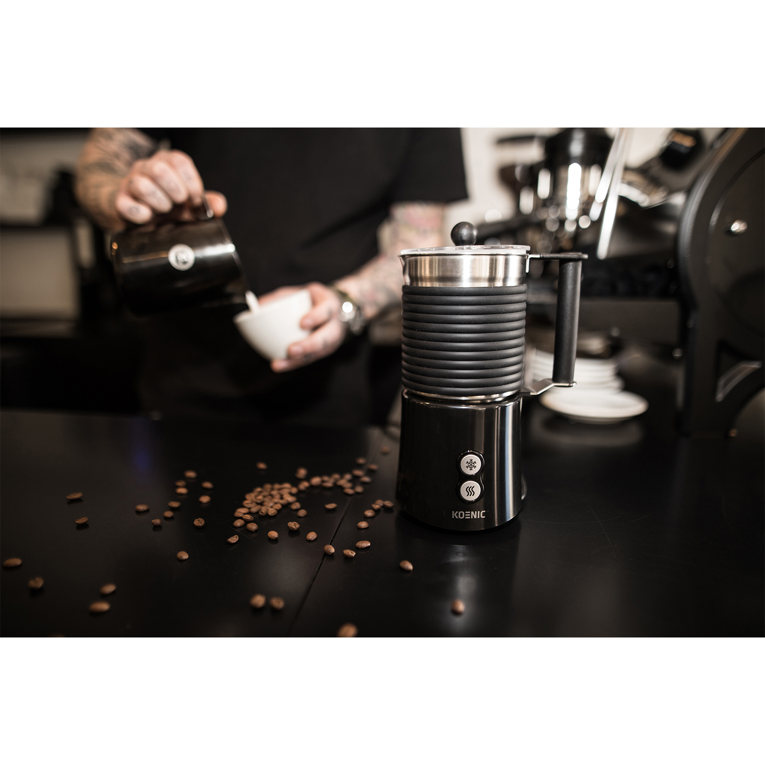 Un barista versa il latte in una tazza con un montalatte Koenic sullo sfondo.