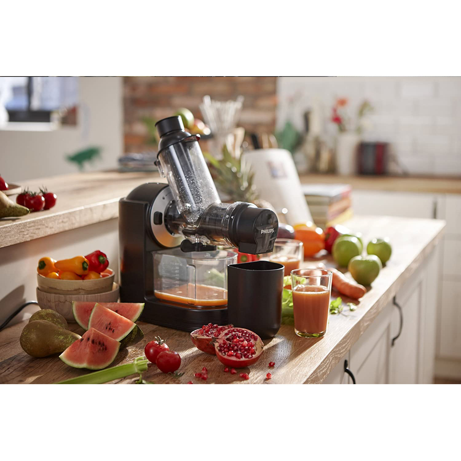 Un estrattore di succo con ingredienti come anguria, mele e melograno su un tavolo.