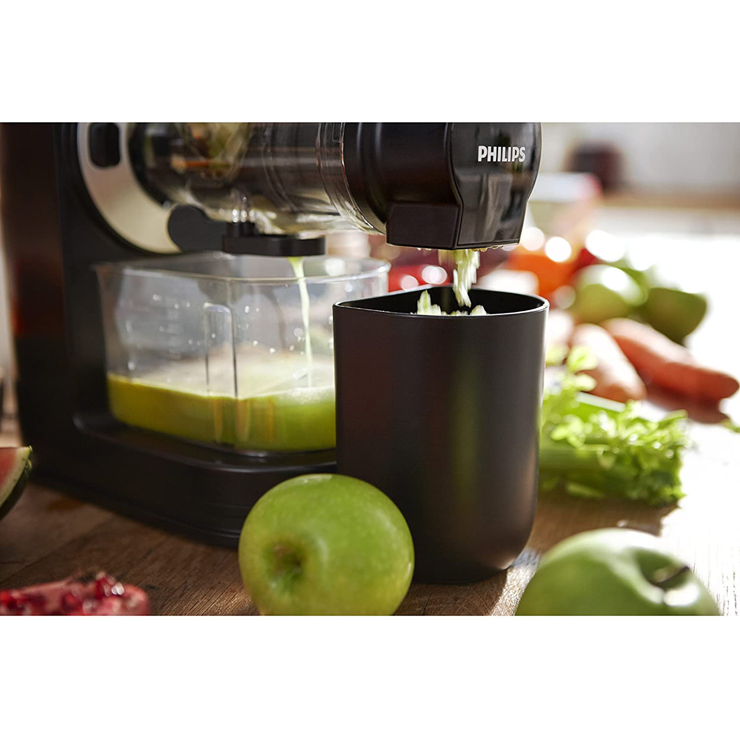 Estrattore di succo in azione, versa succo in un contenitore, con mele verdi e verdure.